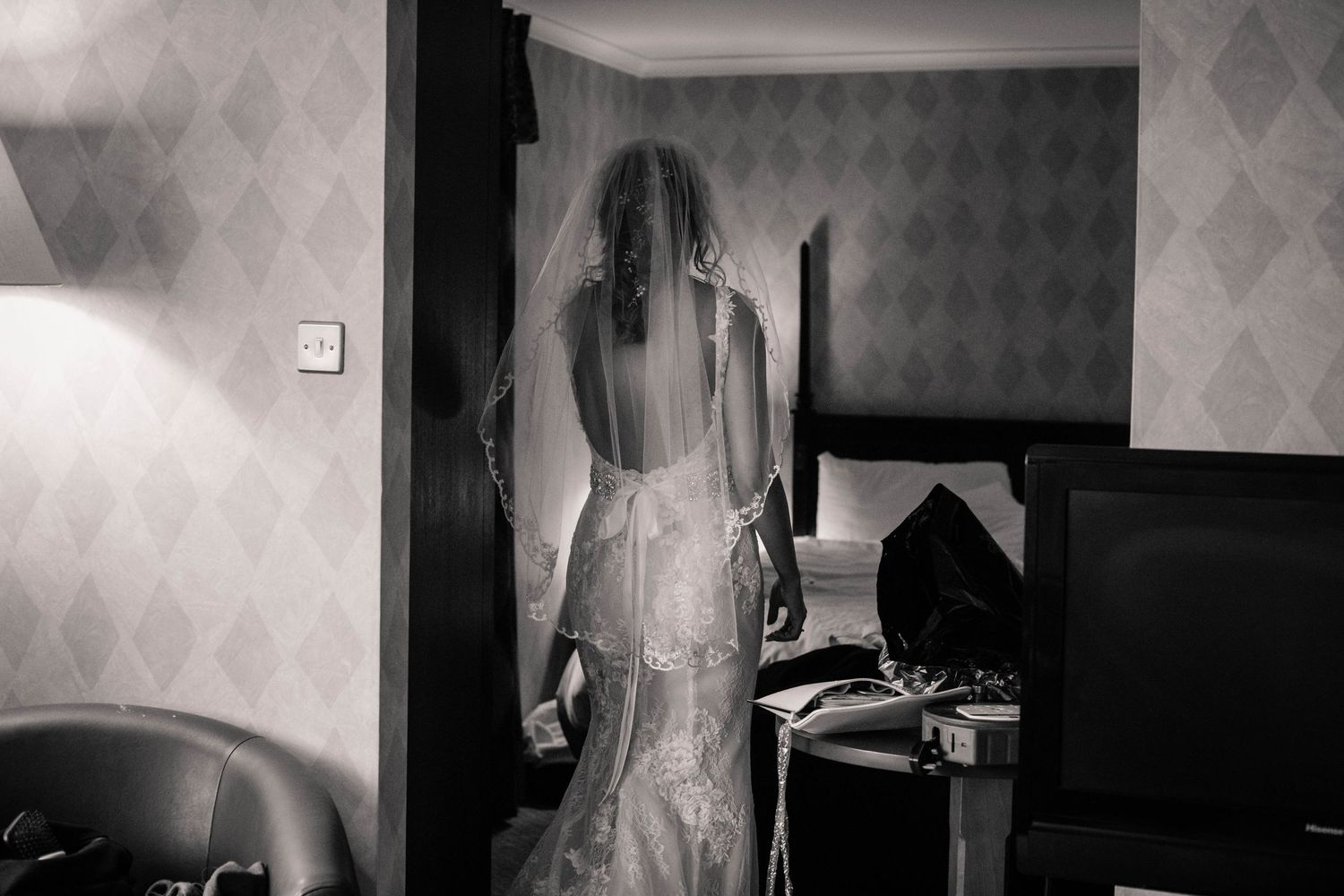 Black-and-white portrait of a bride looking out of a window before her ceremony