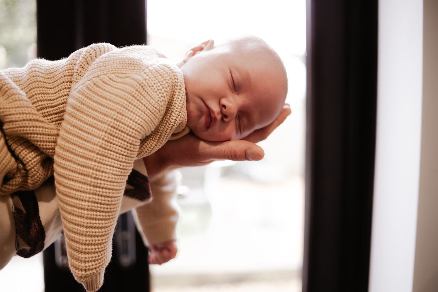 Father gently cradling her newborn baby beside a window