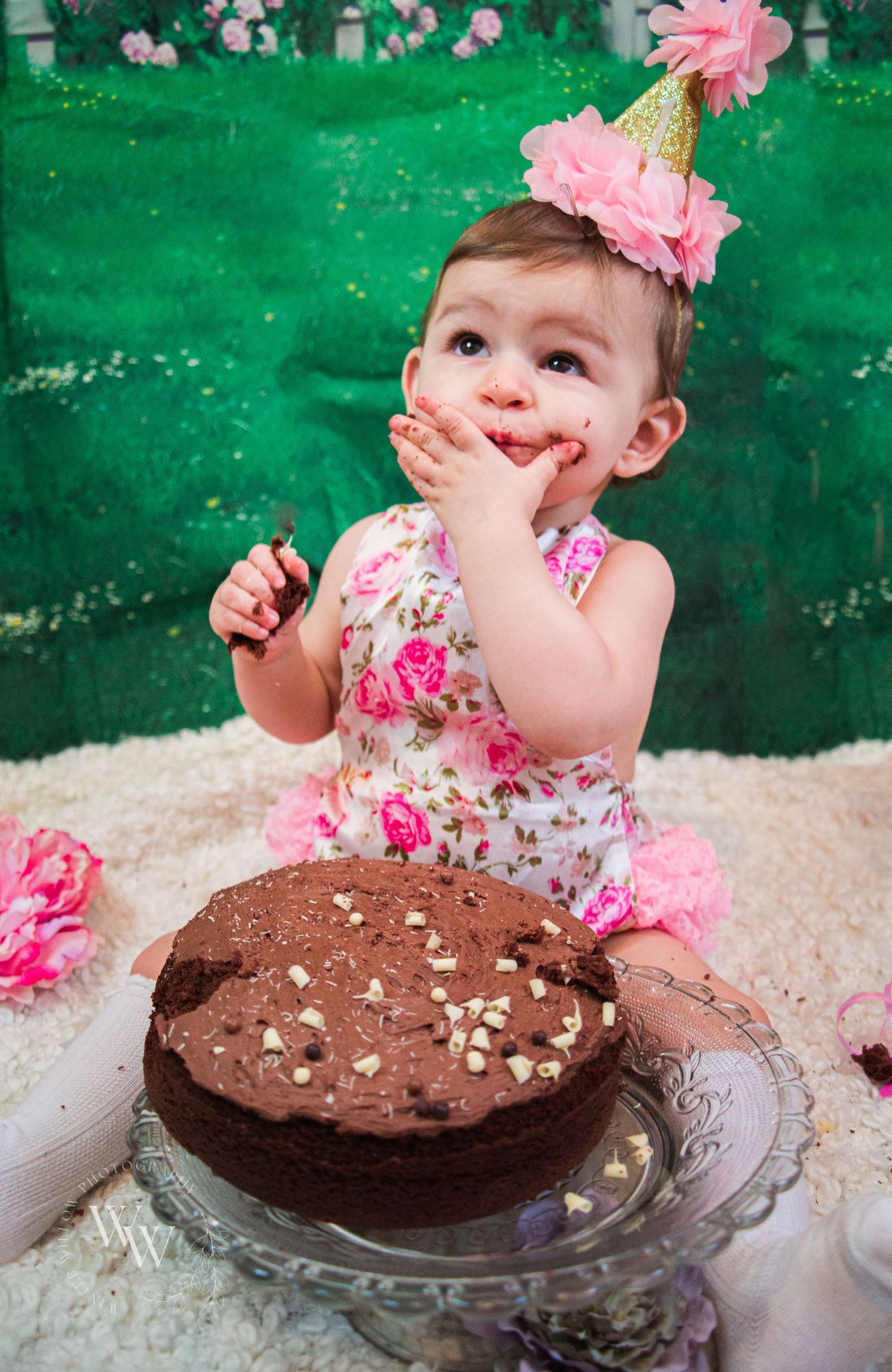 One-year-old girl smiling with chocolate-covered fingers during her cake smash
