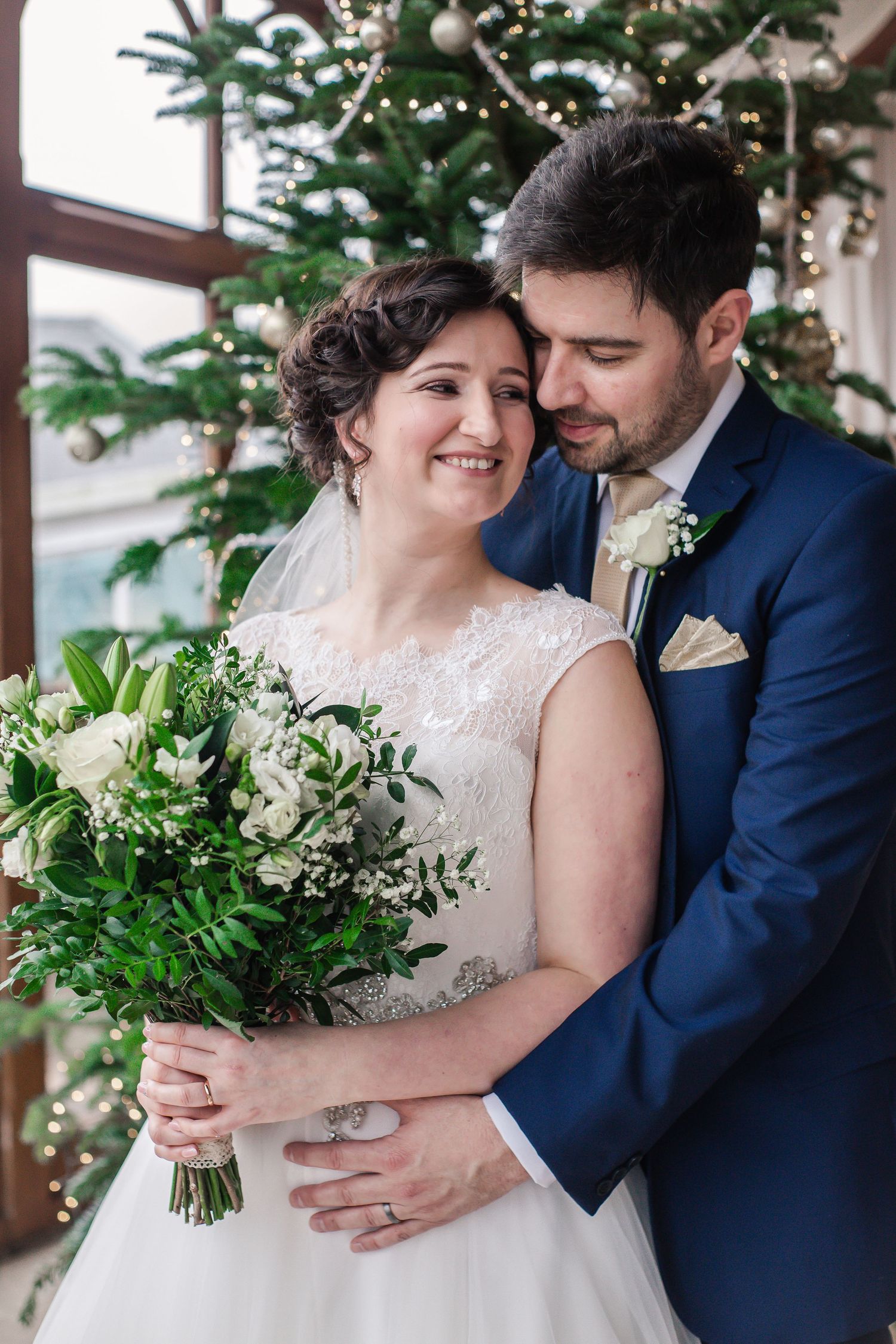 Bride and groom sharing a close embrace beside conservatory windows inside Craig y Nos Castle
