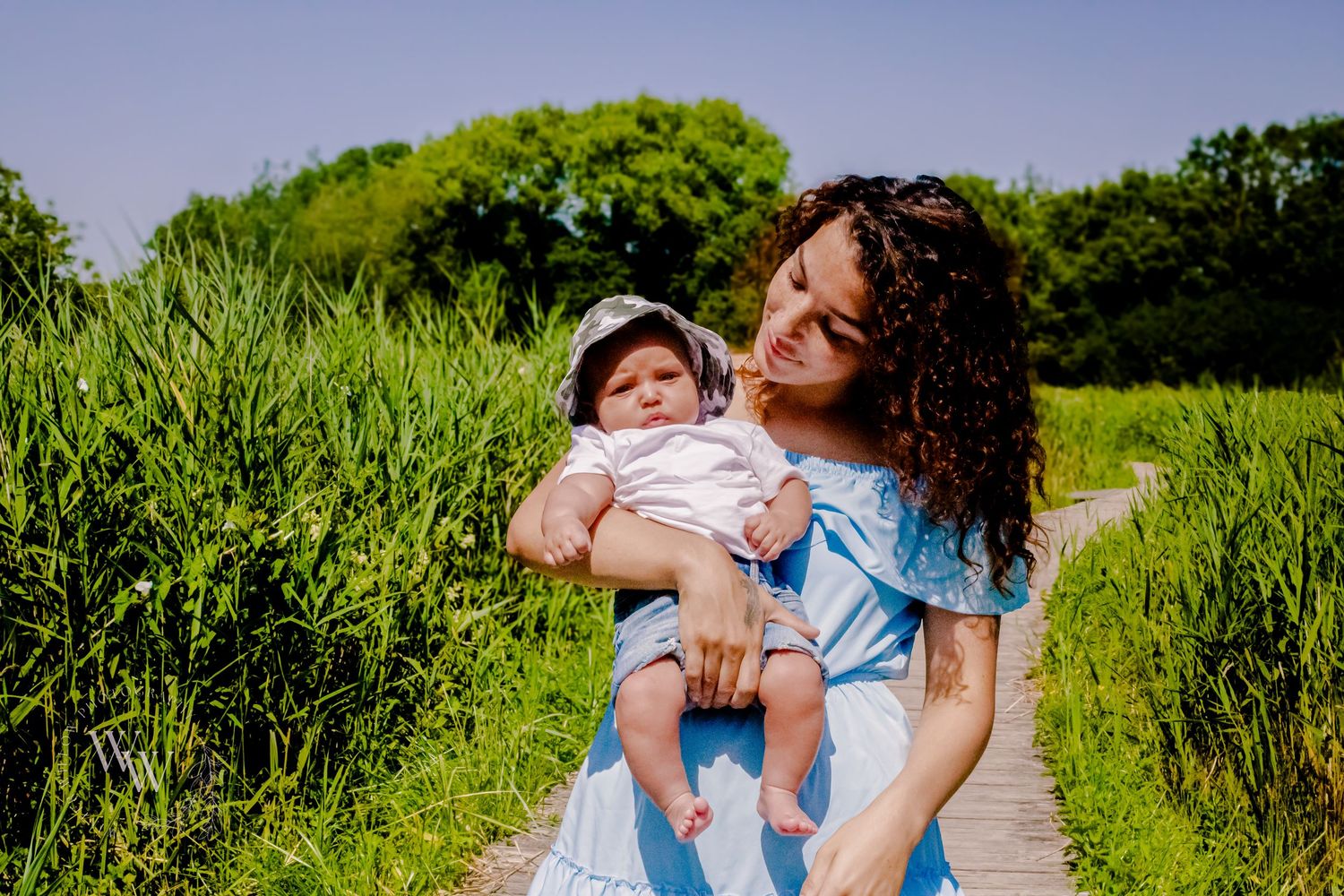 Mother smiling at her baby beside tall summer greenery at Cosmeston Lake, Penarth