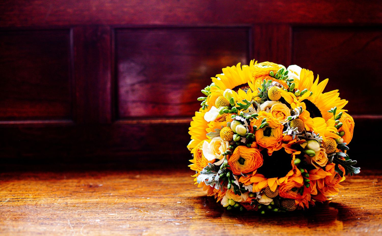 Orange and yellow sunflower wedding bouquet displayed against dark wood