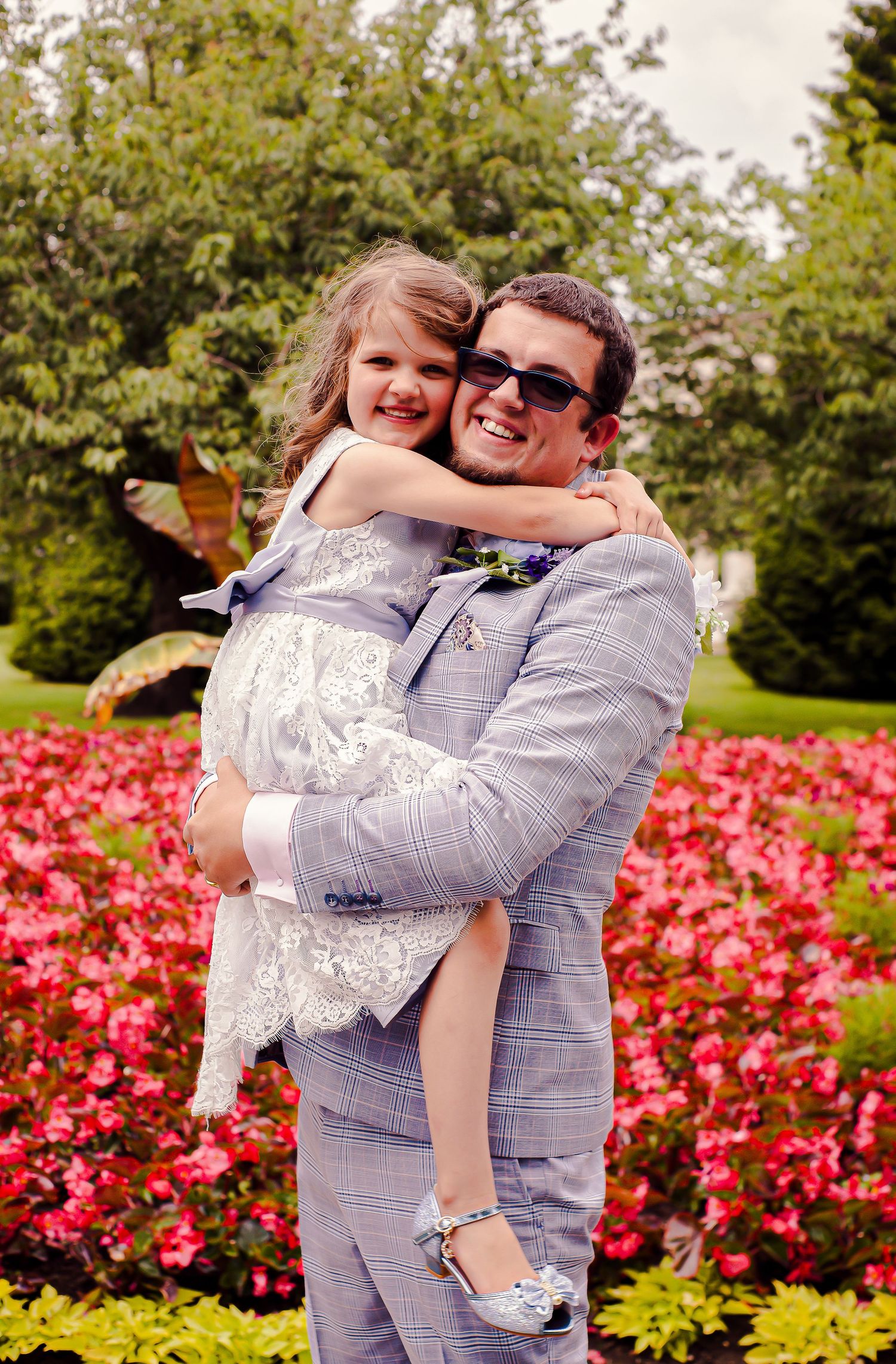 Groom holding a young wedding guest beside the colourful flower beds, in Sophia Gardens