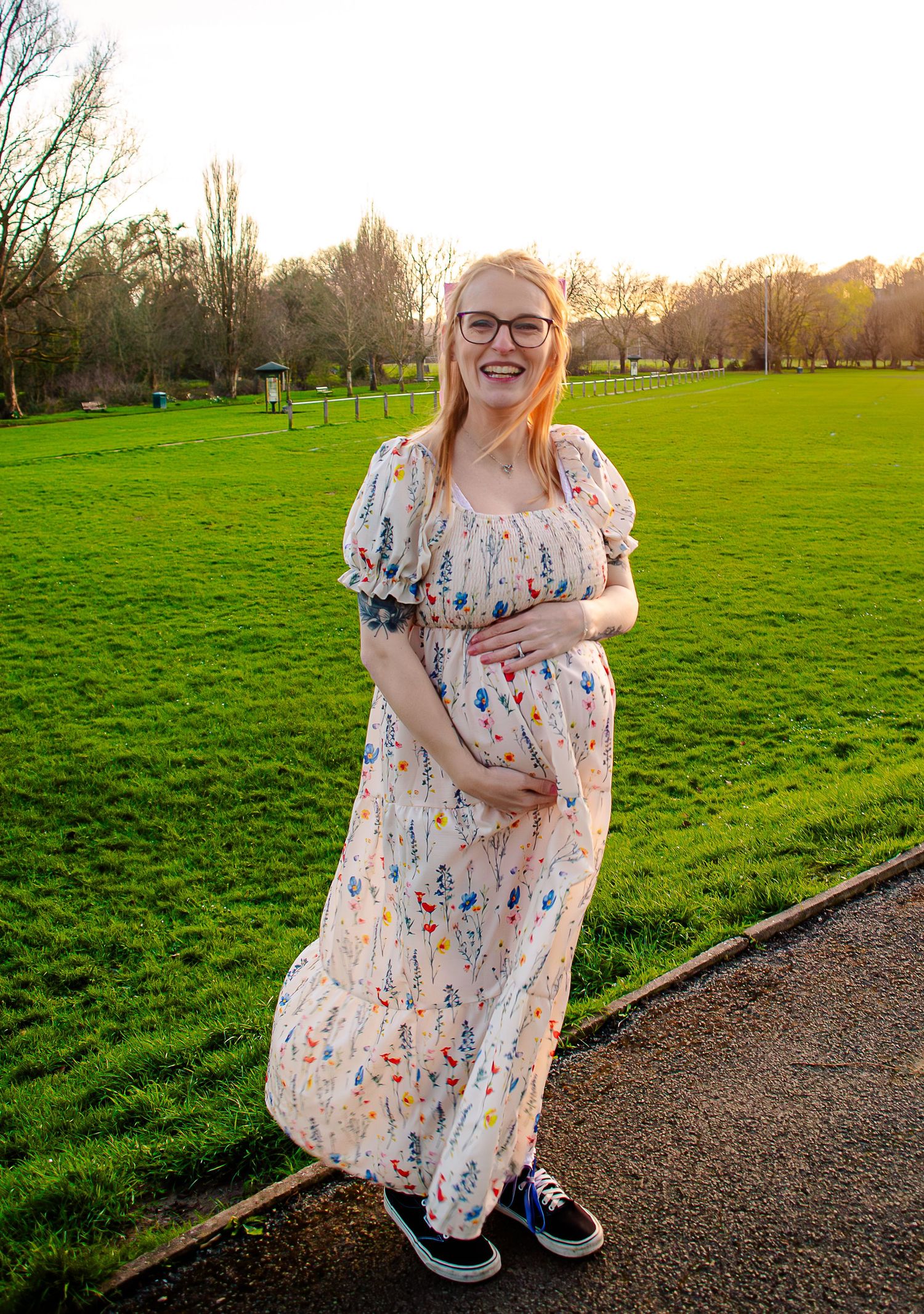 Expectant mother cradling her bump in a floral dress at golden hour