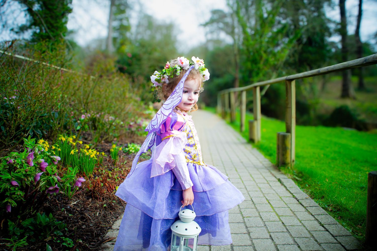 Young girl dressed as a fairy walking along a flower-lined garden path