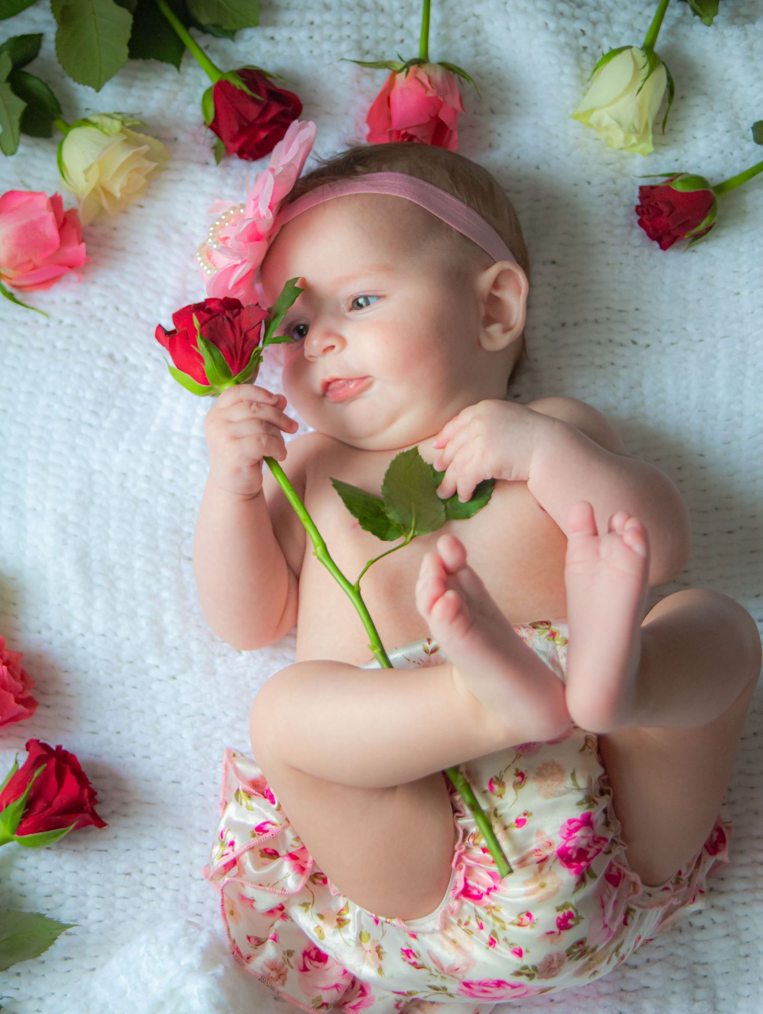 Baby girl holding a pink rose during a floral milestone session