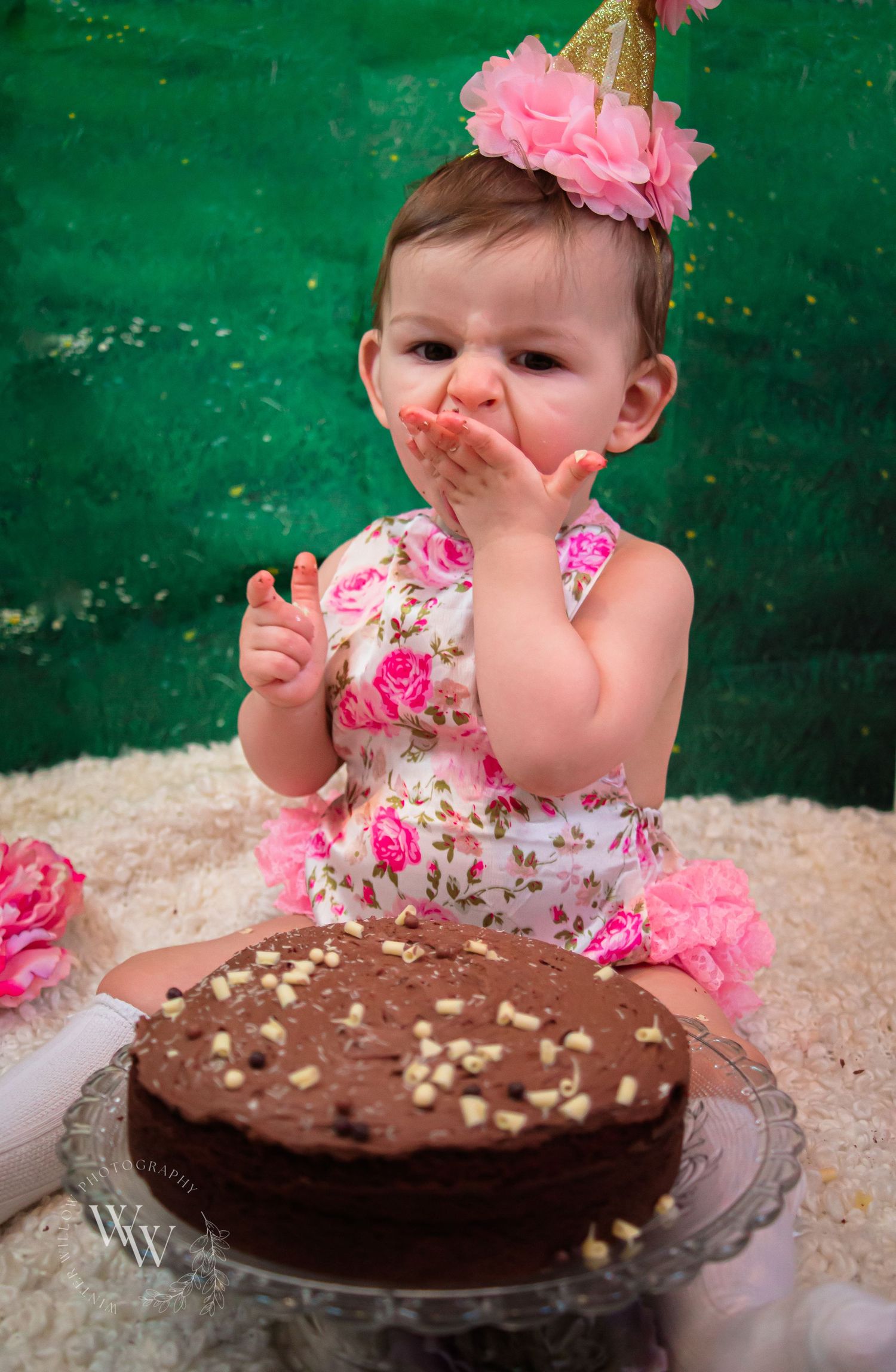Happy baby girl laughing beside her first-birthday chocolate cake