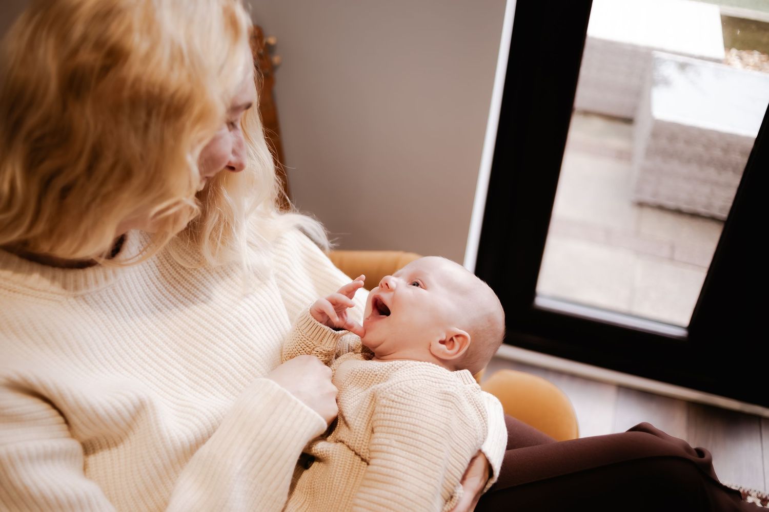 Mother gently cradling her newborn baby beside a window