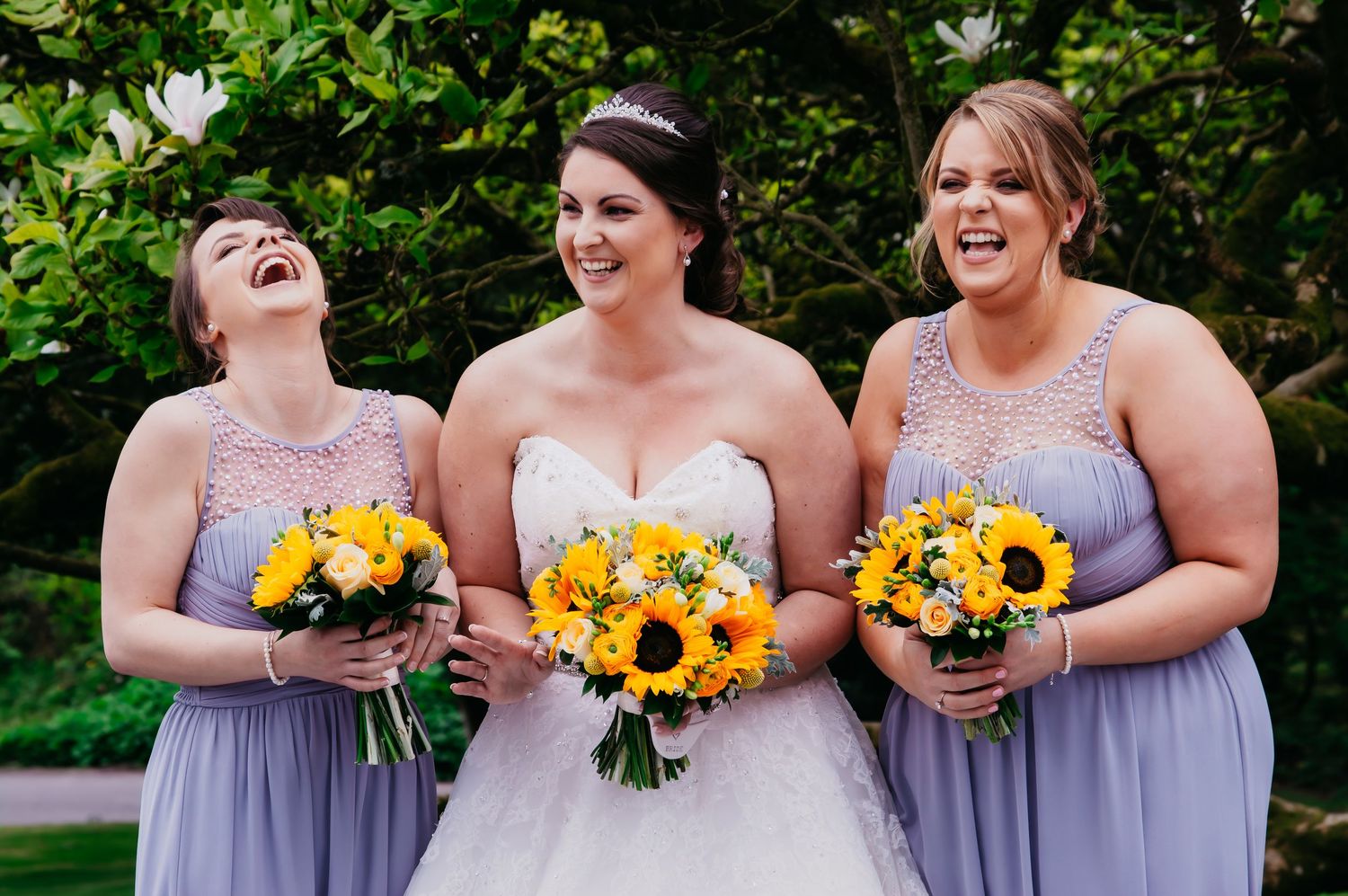 Bride laughing with her bridesmaids while holding bright sunflower wedding bouquets