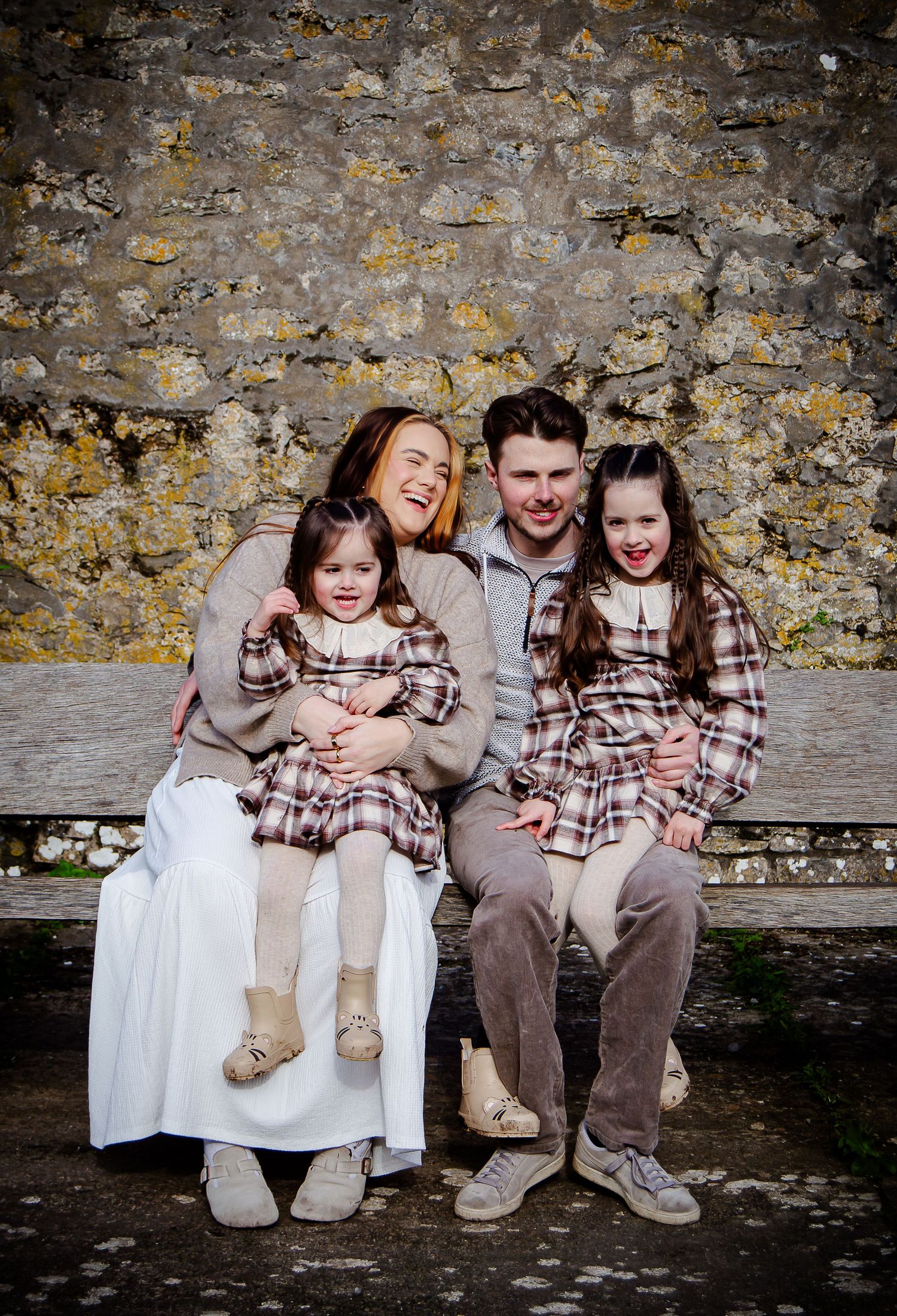 Family of four sitting together beside a stone wall at Southerndown