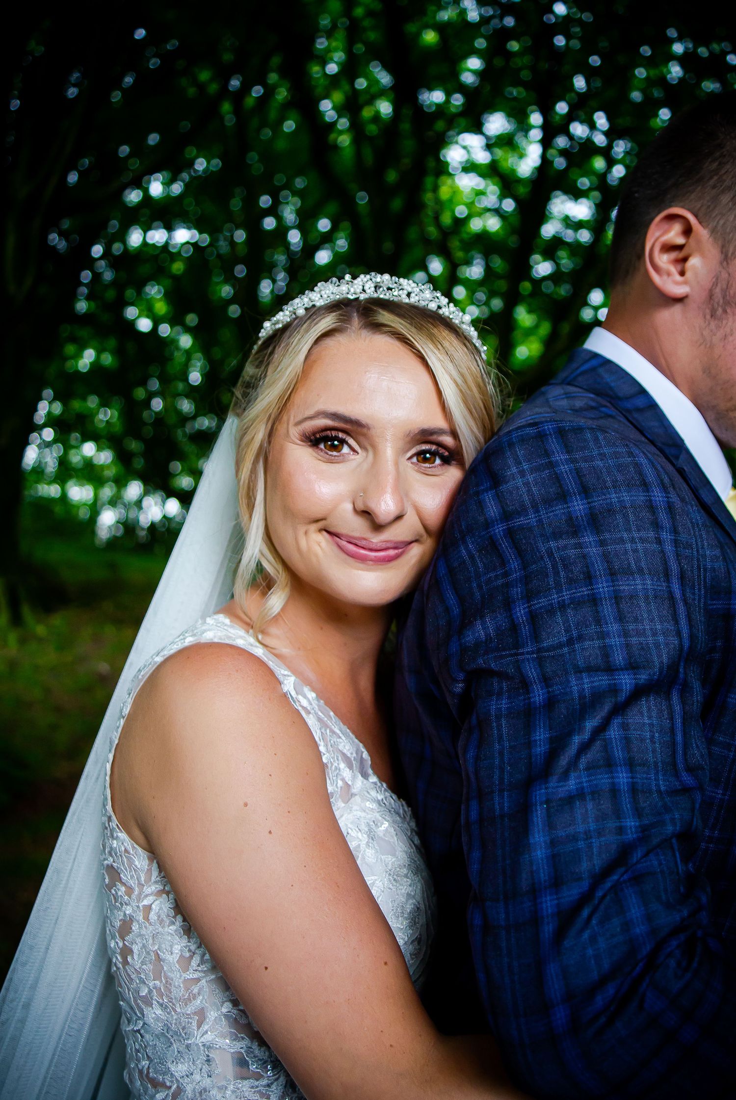 Bride smiling while embracing her groom in the woodland at Ridgeway Golf Club