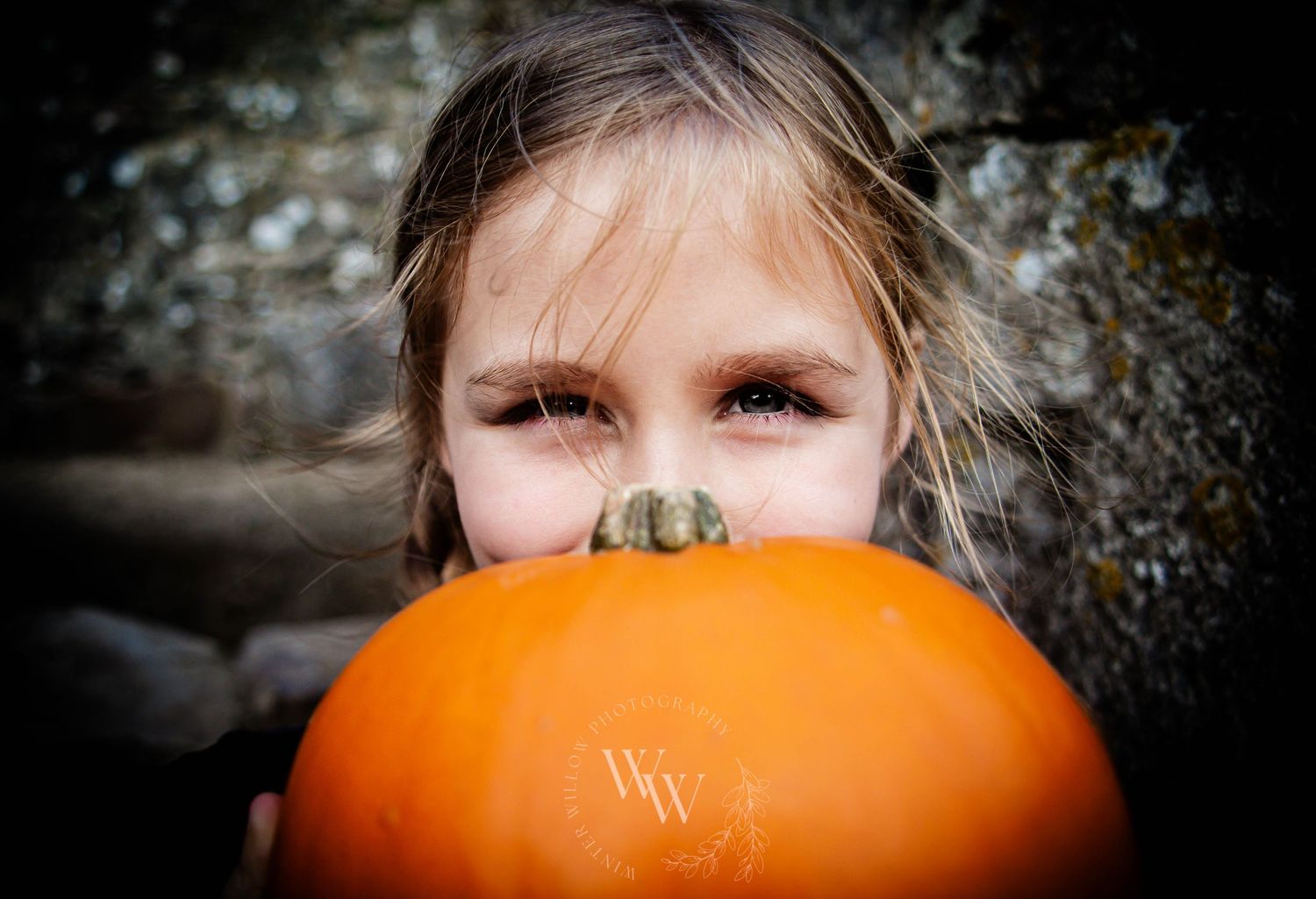 Child peeking over a pumpkin during an autumn portrait session