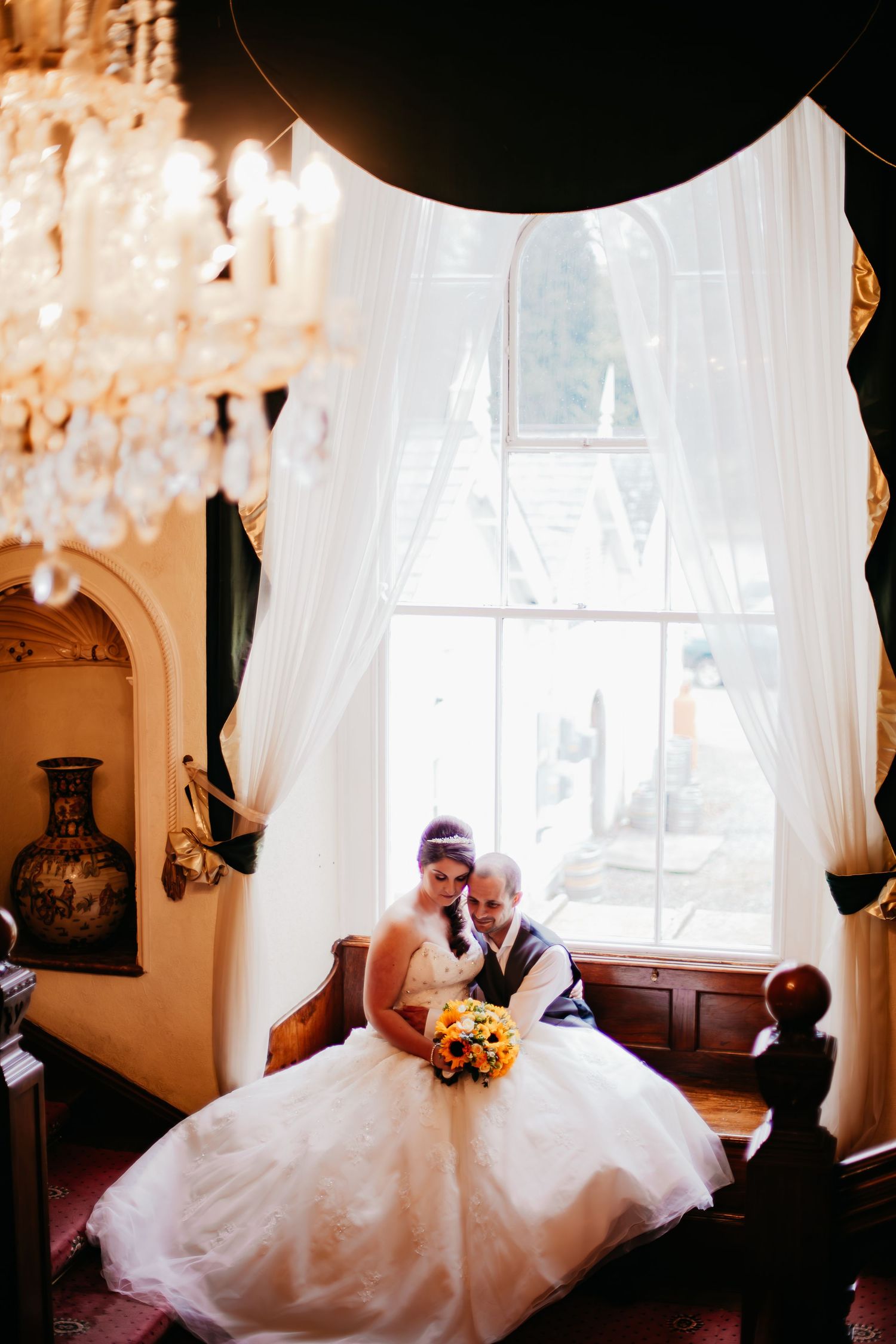 Bride seated beside a bright window holding her sunflower wedding bouquet