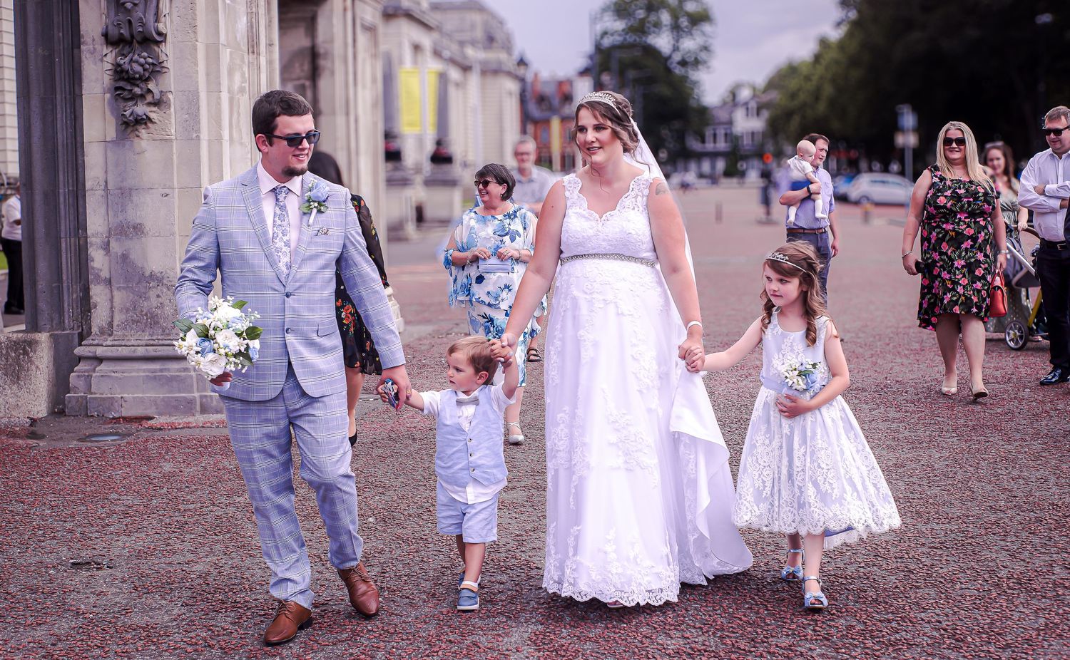 Newlyweds walking through Cardiff city hall, with three young wedding guests