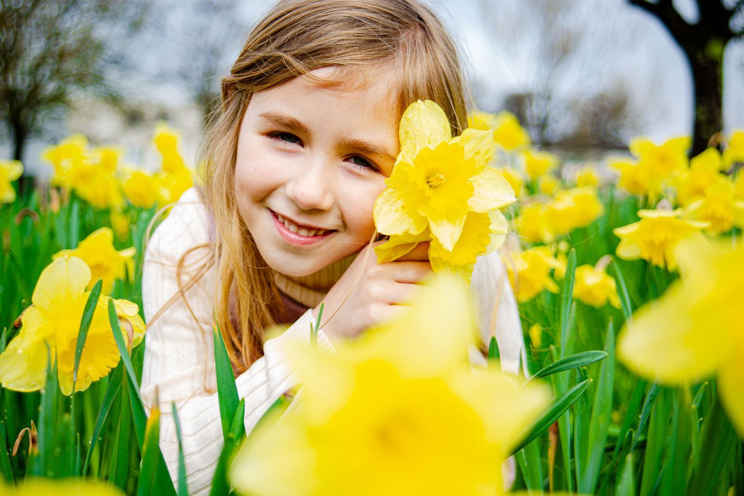 Smiling girl holding a daffodil beside her face