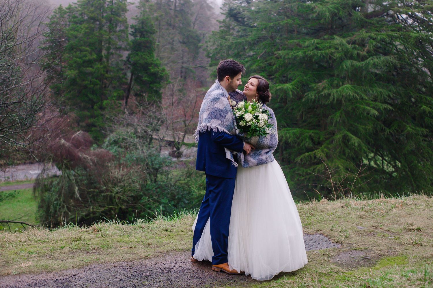 Bride and groom wrapped together in a blanket during woodland wedding portraits