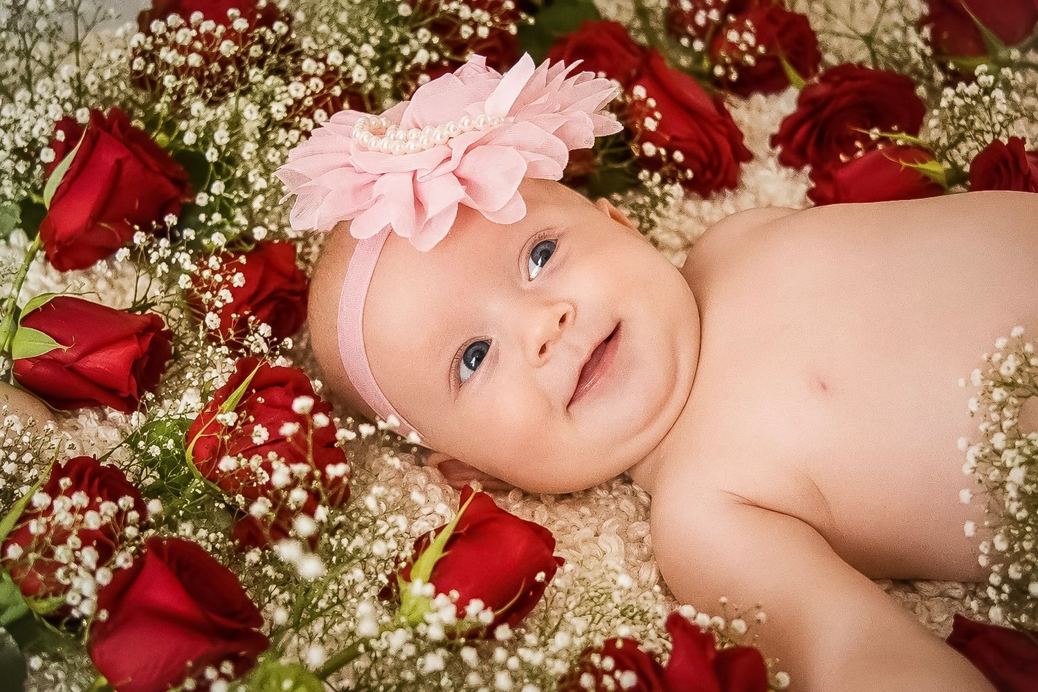 Close-up of a smiling baby girl lying among red roses and gypsophila