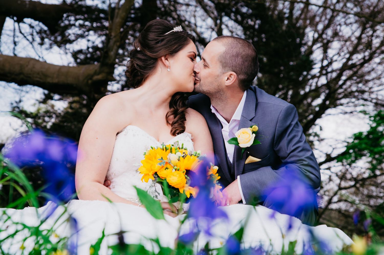 Newlywed couple sharing a kiss among purple spring flowers