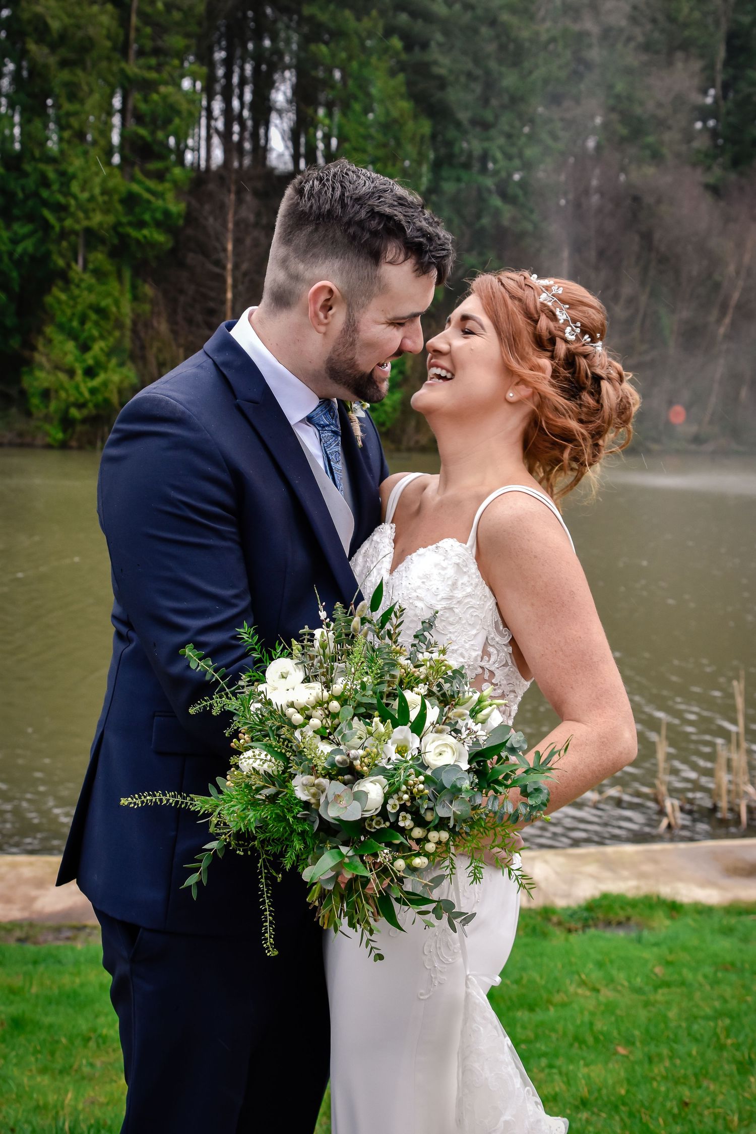Bride and groom kissing while holding a white and green wedding bouquet