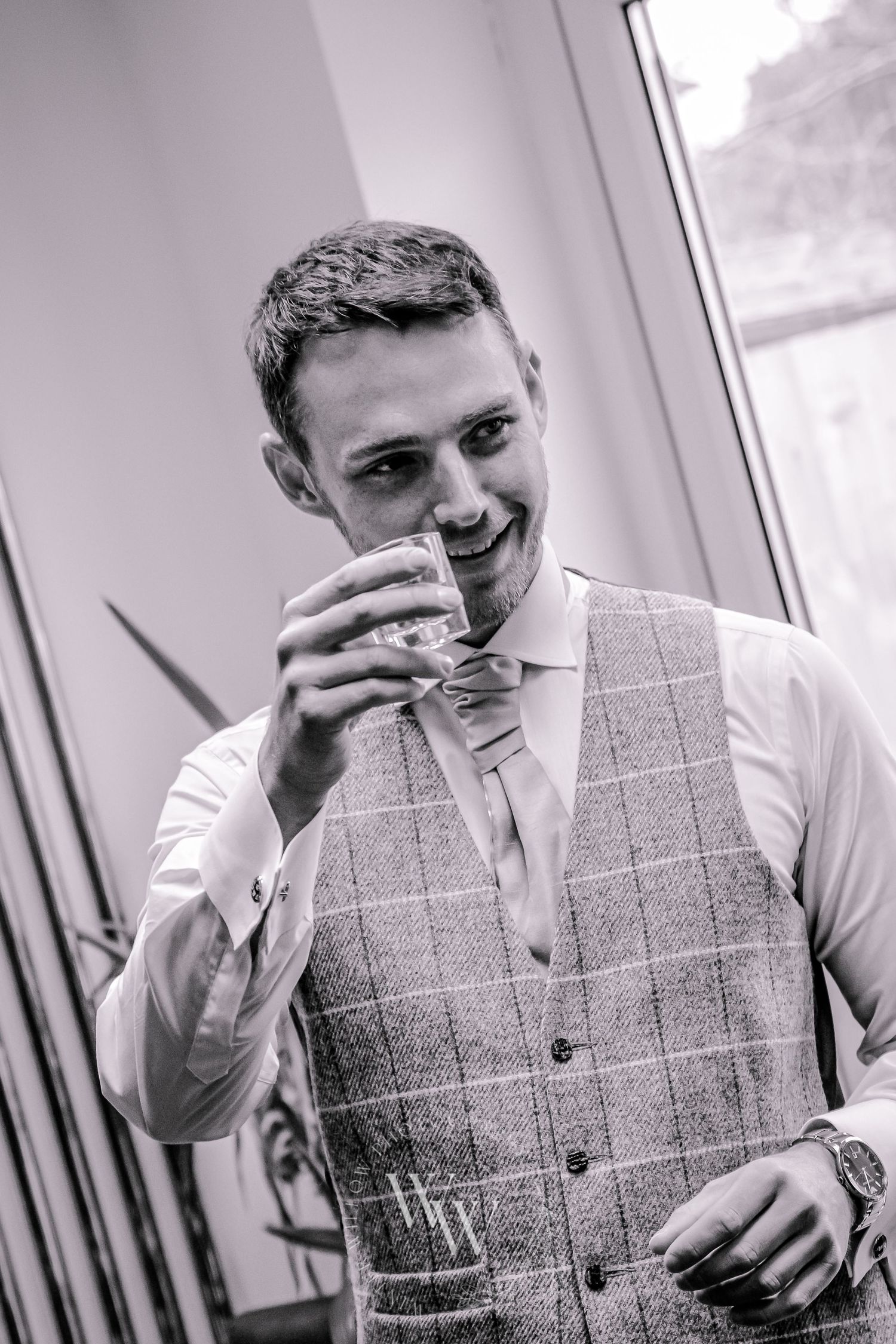 Black and white portrait of the groom enjoying a drink before the wedding