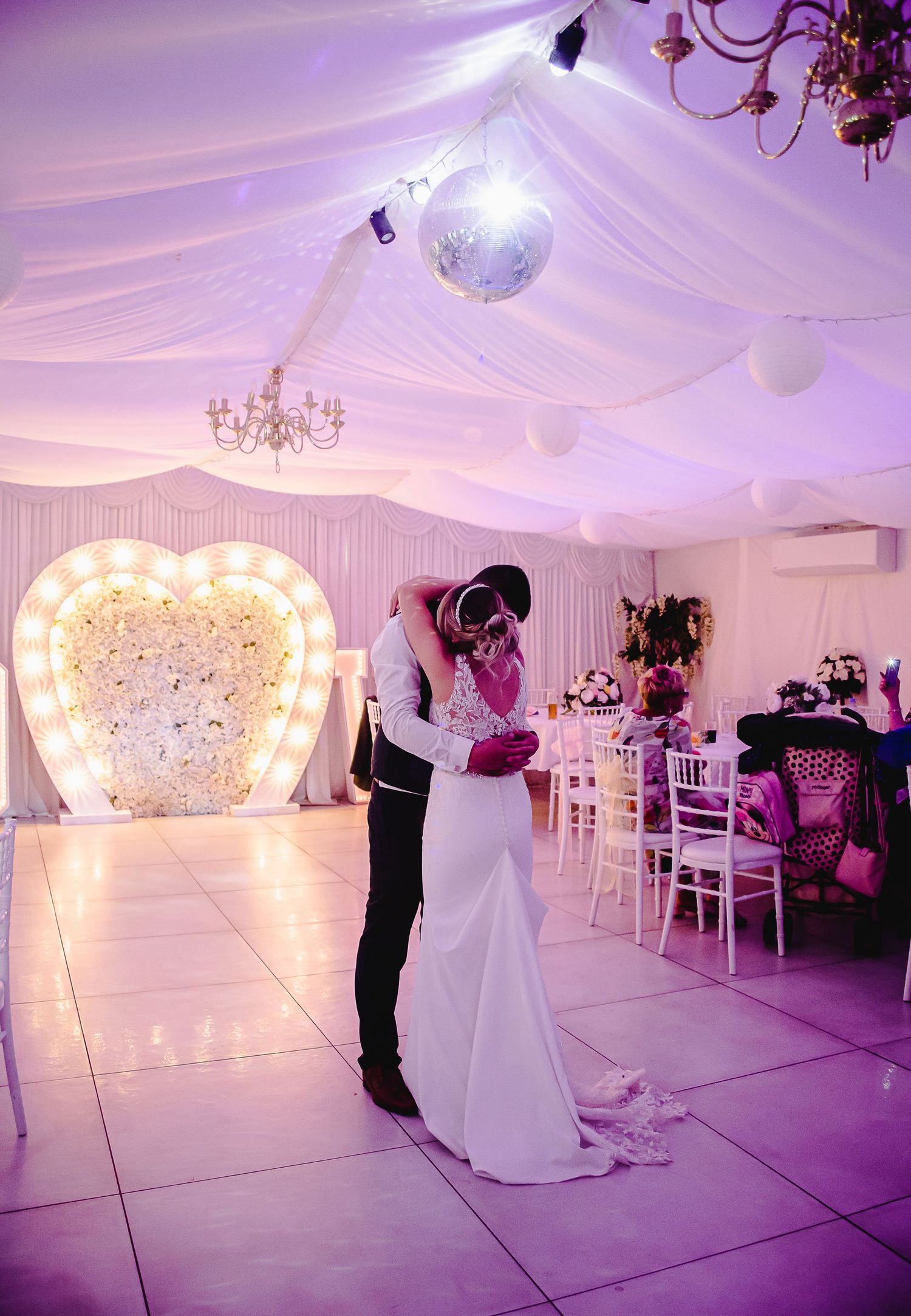 Newly married couple dancing beneath draped lights at their wedding reception