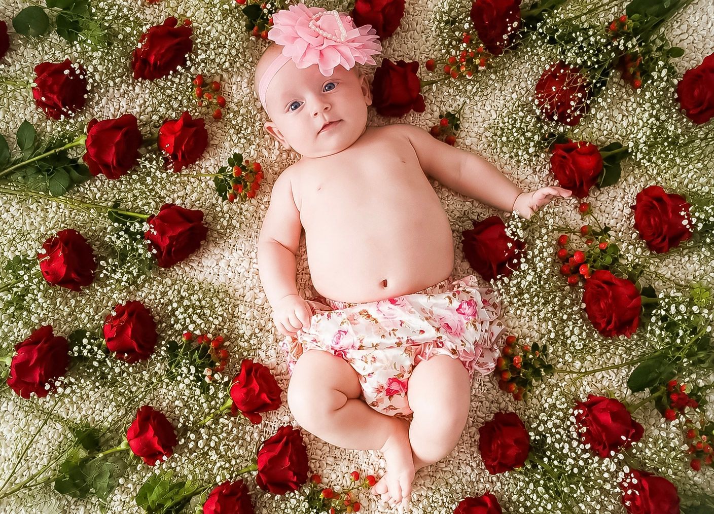 Baby girl lying happily within a heart-shaped arrangement of red roses
