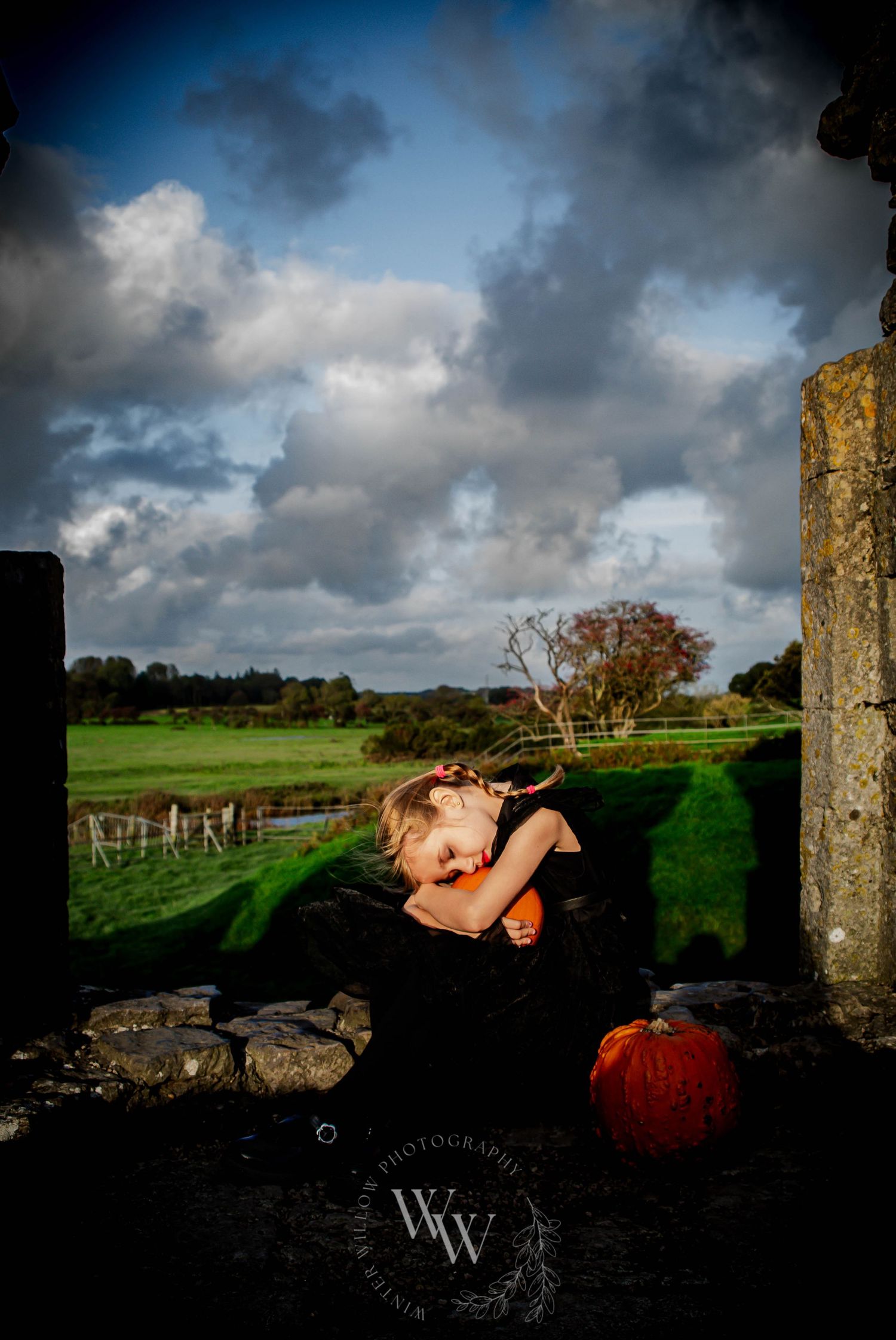 Child sitting beside pumpkins beneath a dramatic autumn sky at Pumpkin Patch PYO Cardiff