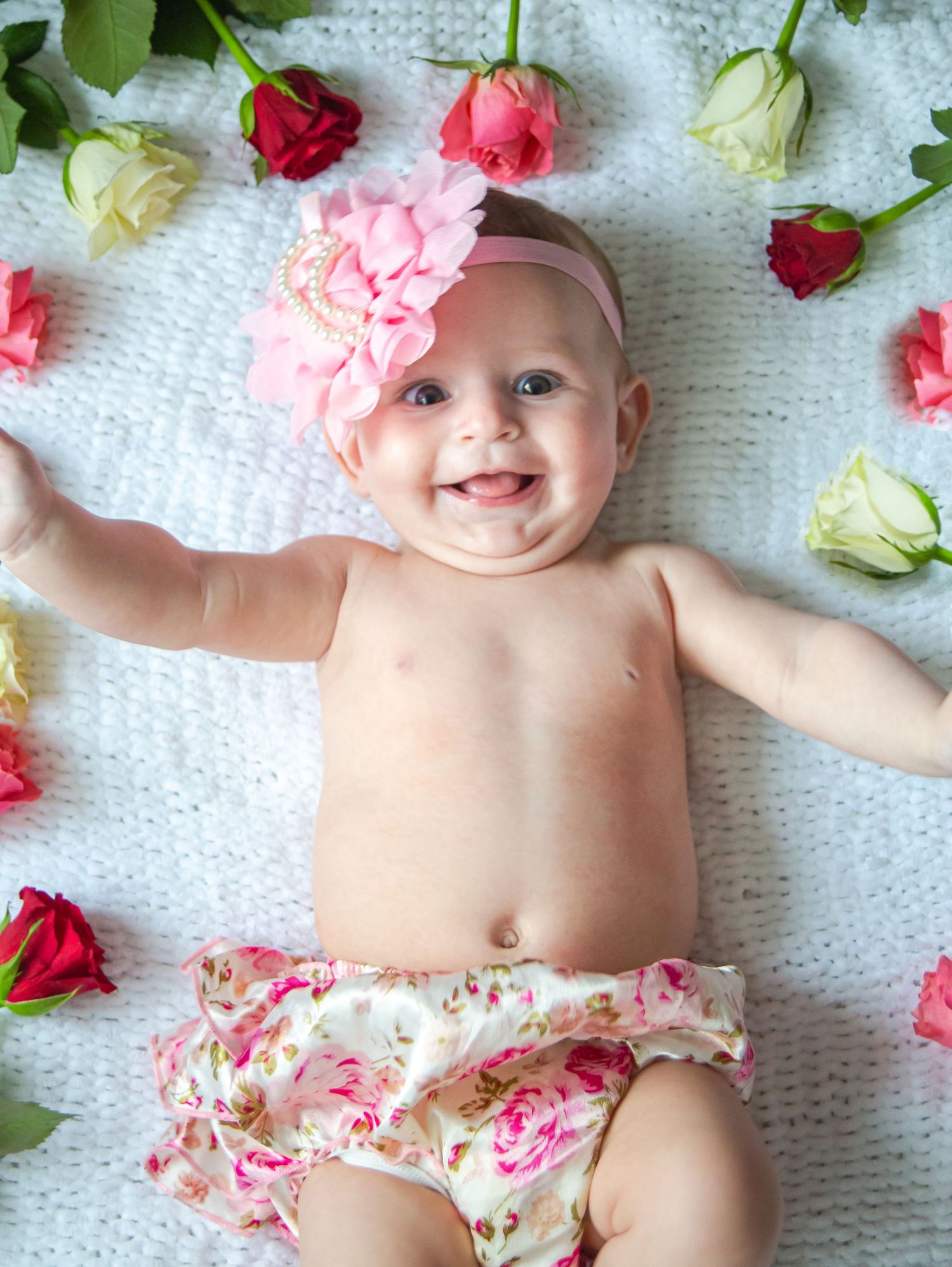 Happy baby girl smiling among colourful rose petals