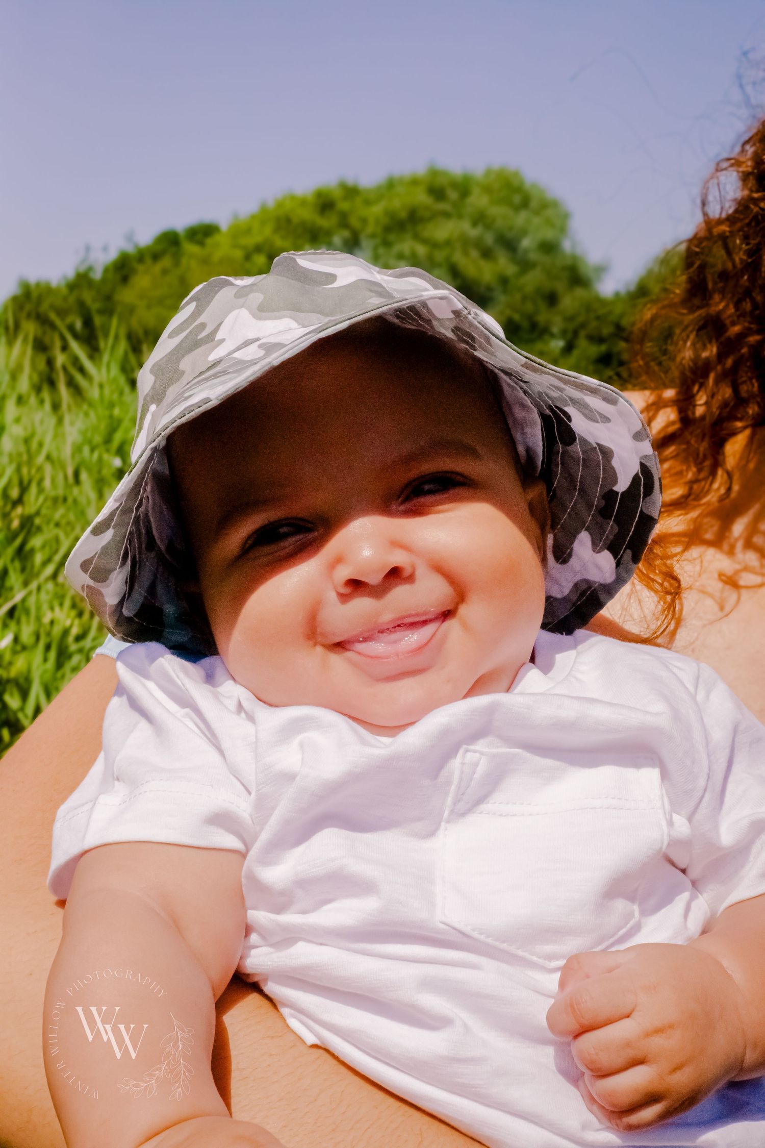 Smiling baby wearing a sun hat during an outdoor family session at Cosmeston Lake, Penarth