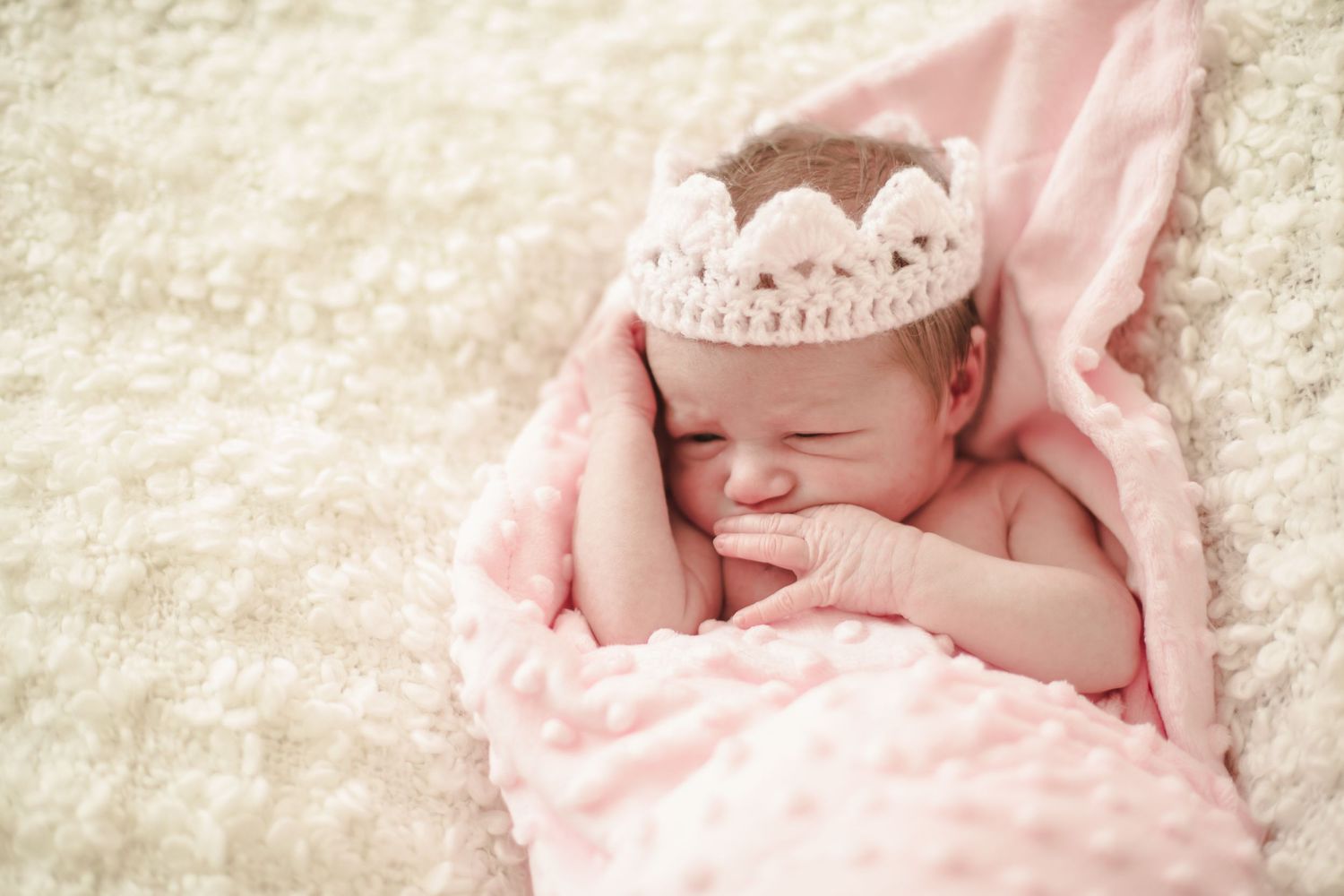 Newborn baby girl wrapped in pink and wearing a knitted crown