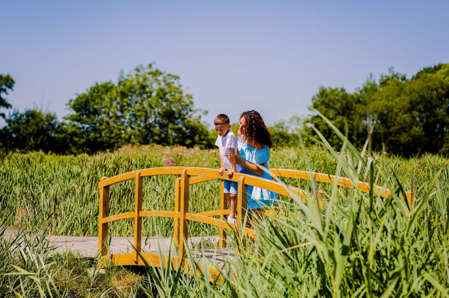 Mother and children crossing a small wooden bridge surrounded by greenery at Cosmeston Lake, Penarth