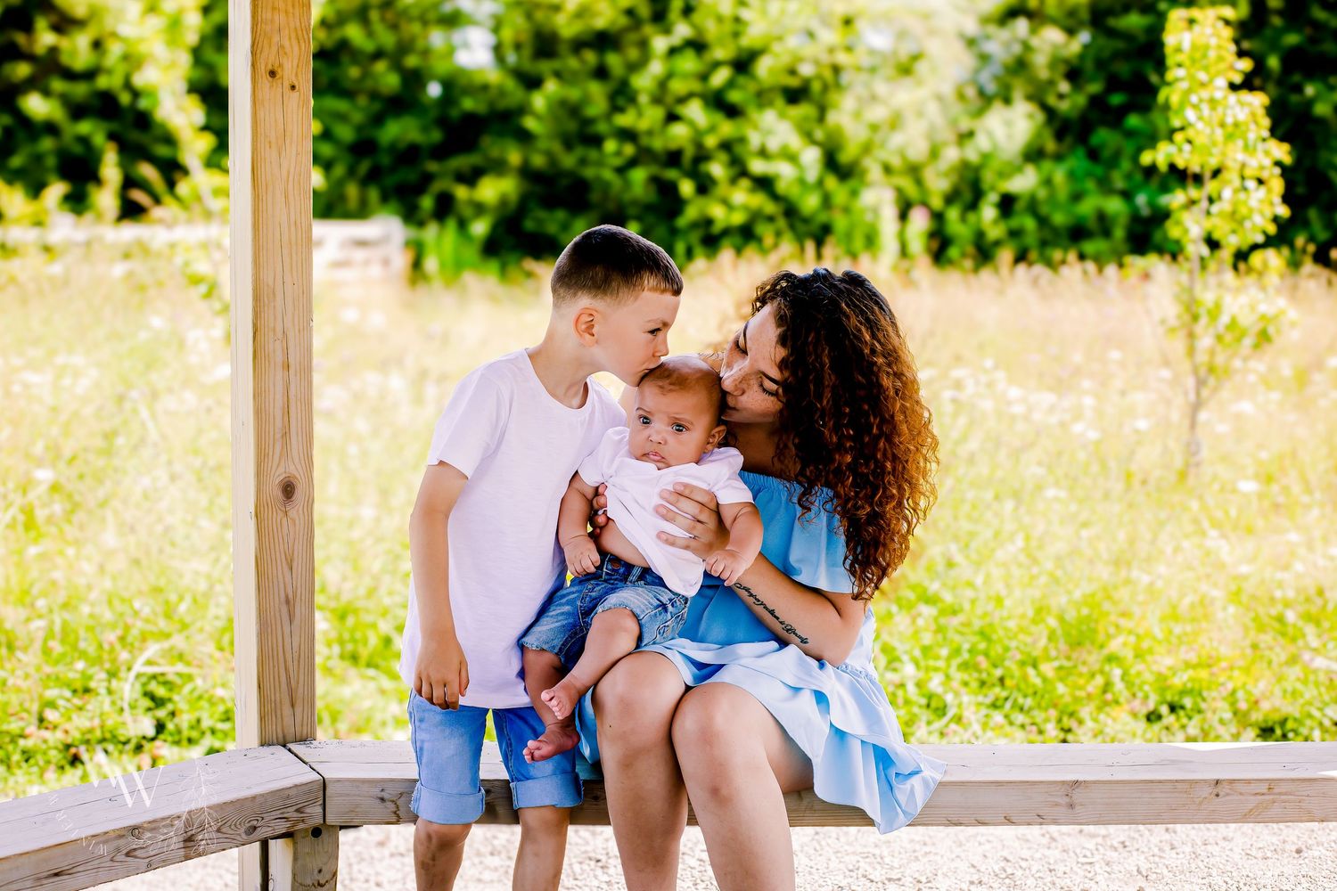 Mother and older sibling kissing baby at Cosmeston Lake in Penarth