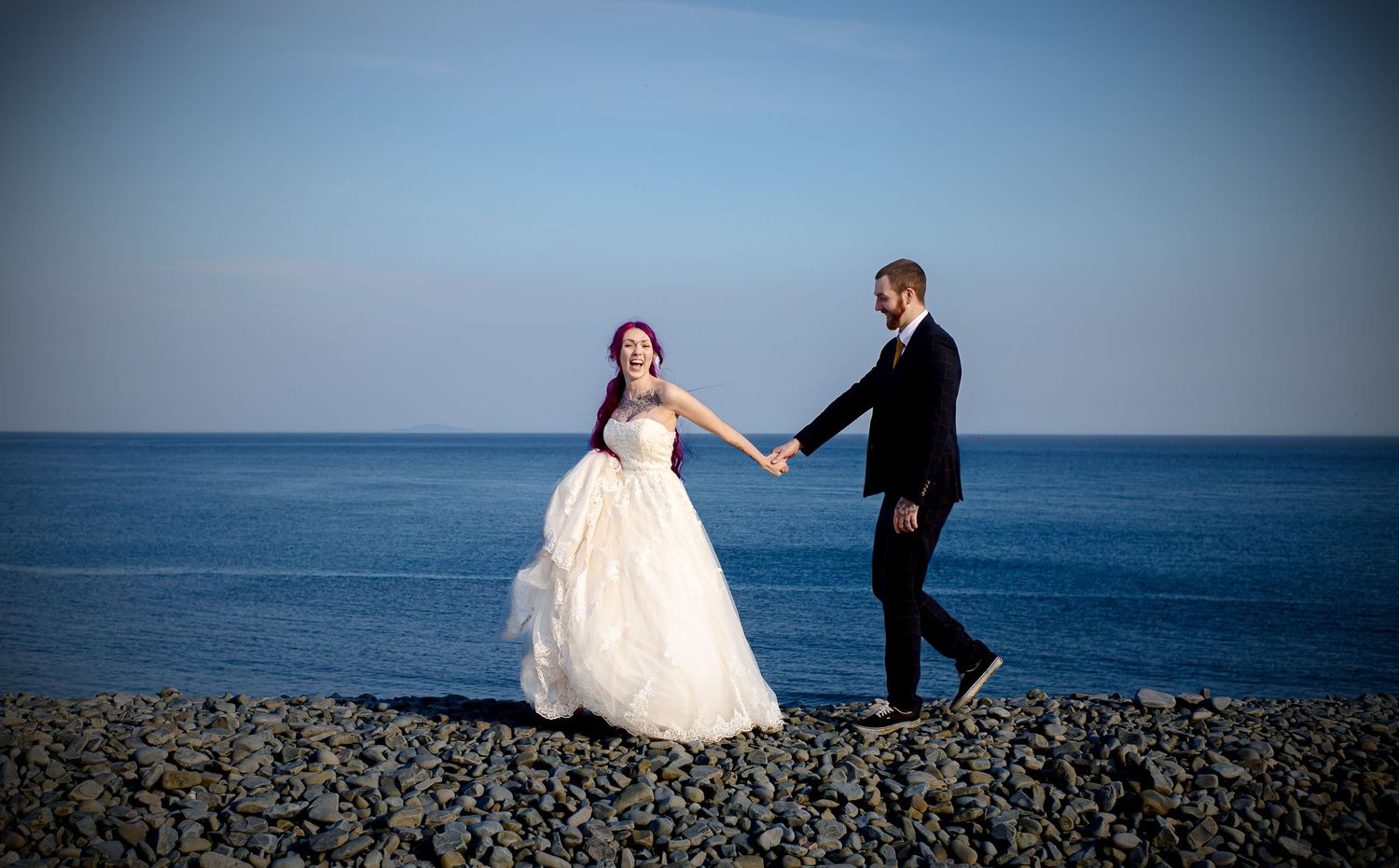 Bride and groom walking hand in hand beside the South Wales coast