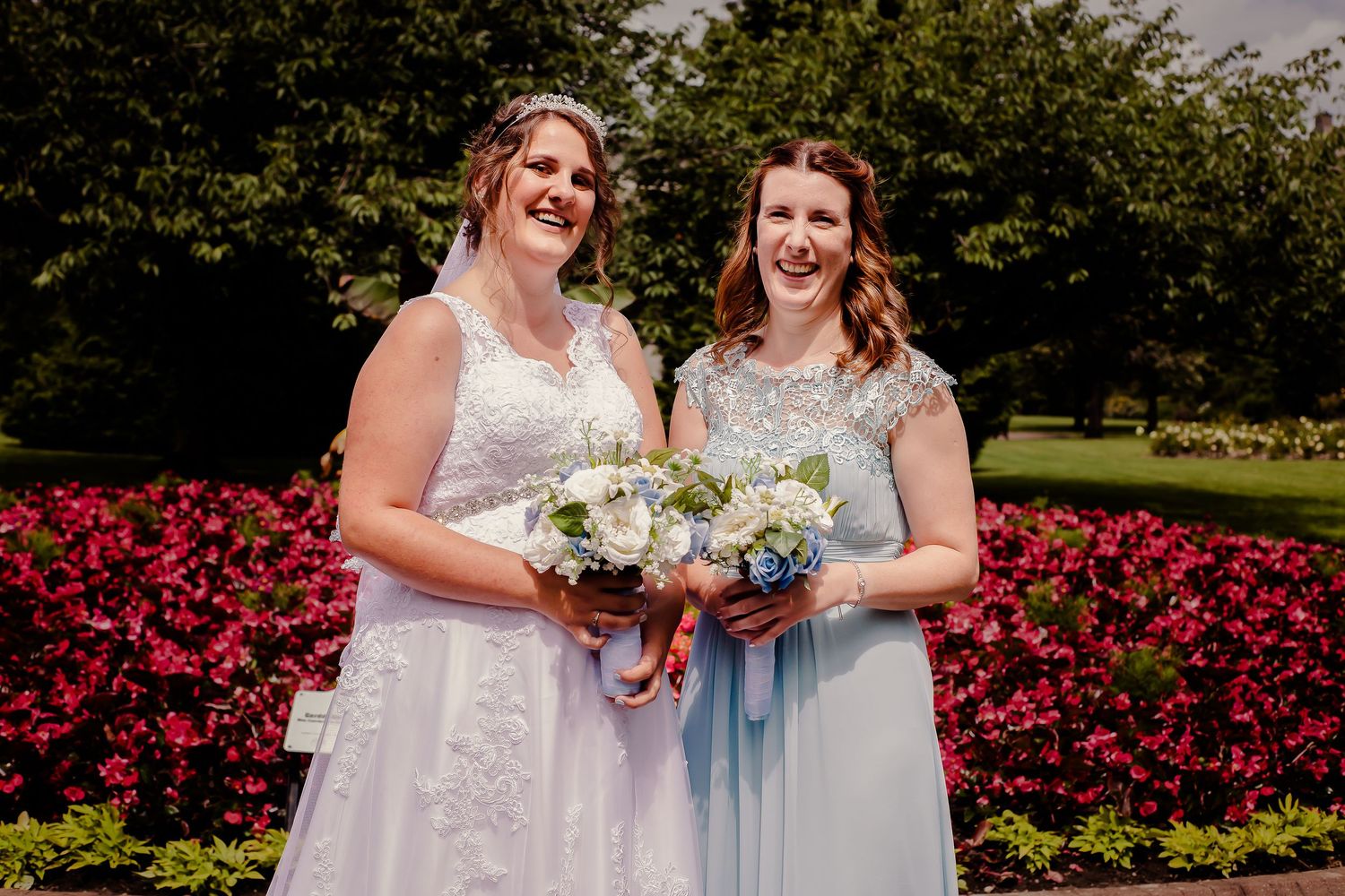 Bride and bridesmaid smiling together with their bouquets in Sophia Gardens