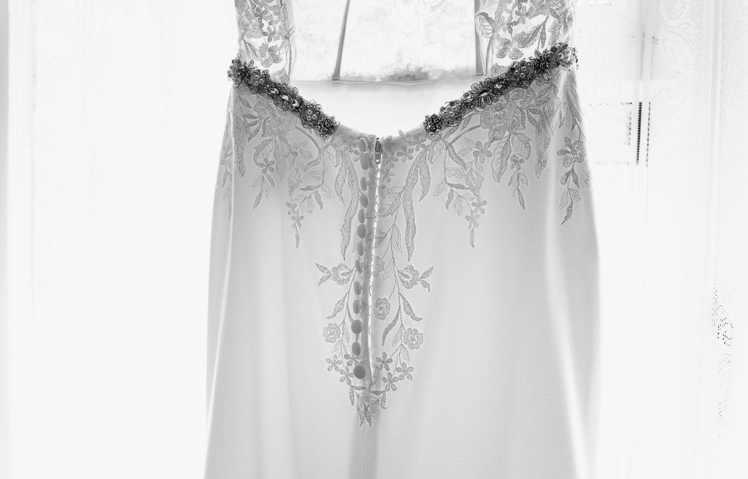 Lace wedding dress hanging in a bright window before the ceremony