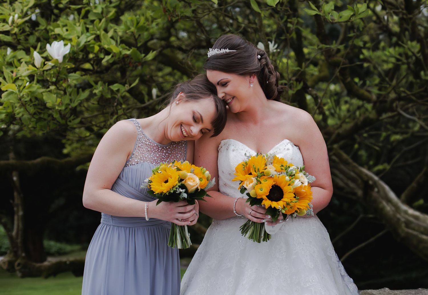 Bridesmiling with her bridesmaid while holding bright sunflower wedding bouquets