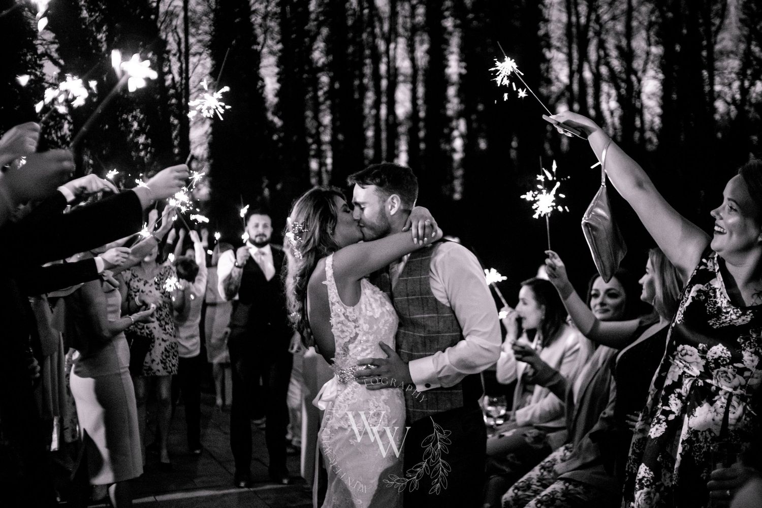 Black and white photograph of newlyweds kissing beneath a sparkler tunnel