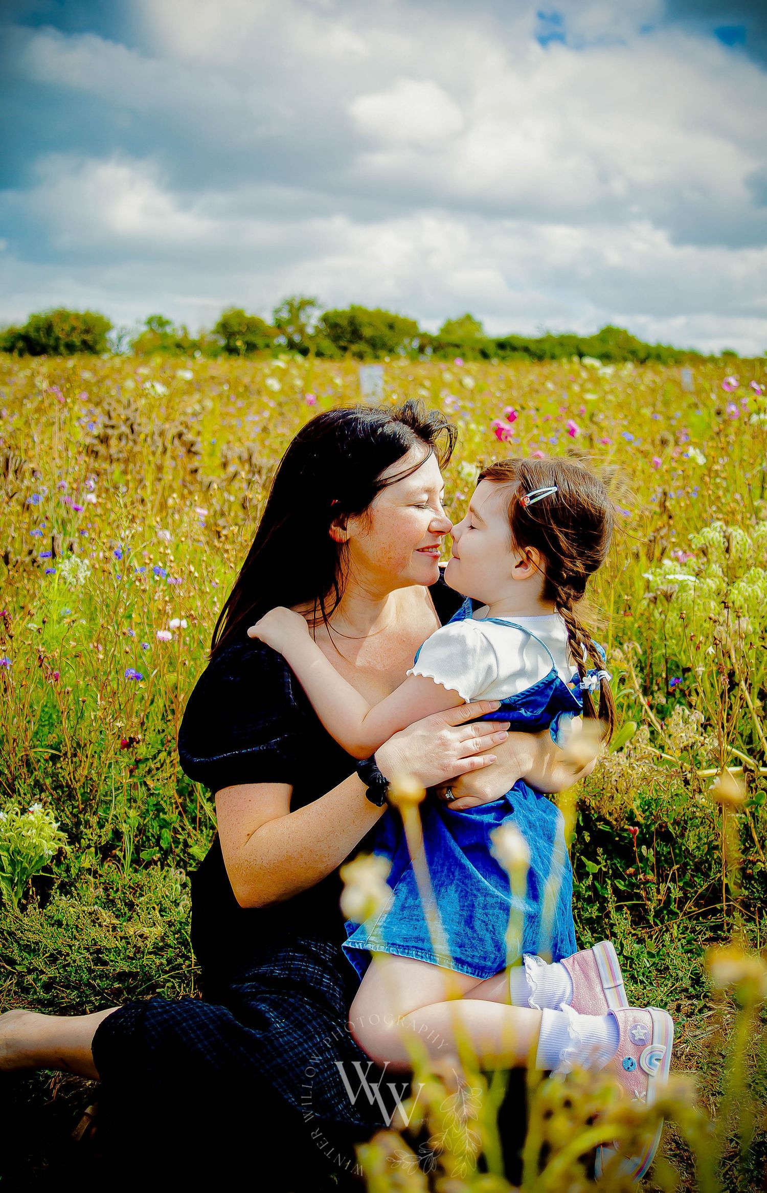 Mother cuddling her baby beside her daughter in a wildflower field