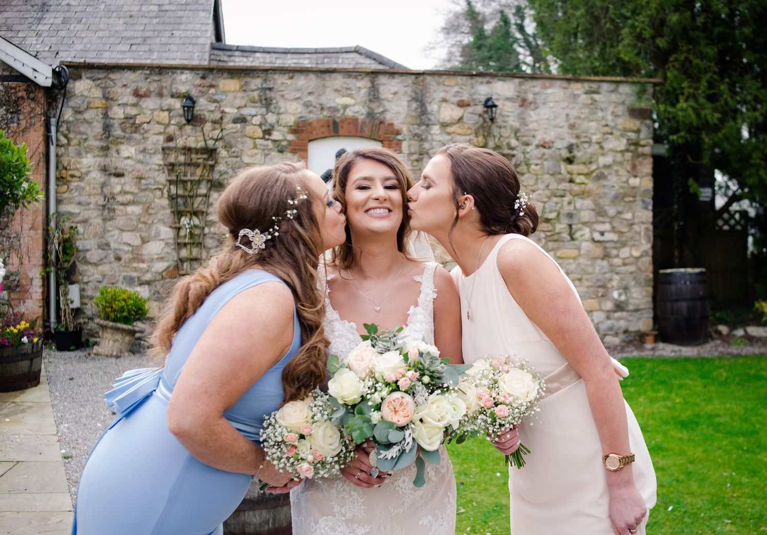 Bride laughing as two bridesmaids kiss her cheeks at Pencoed House