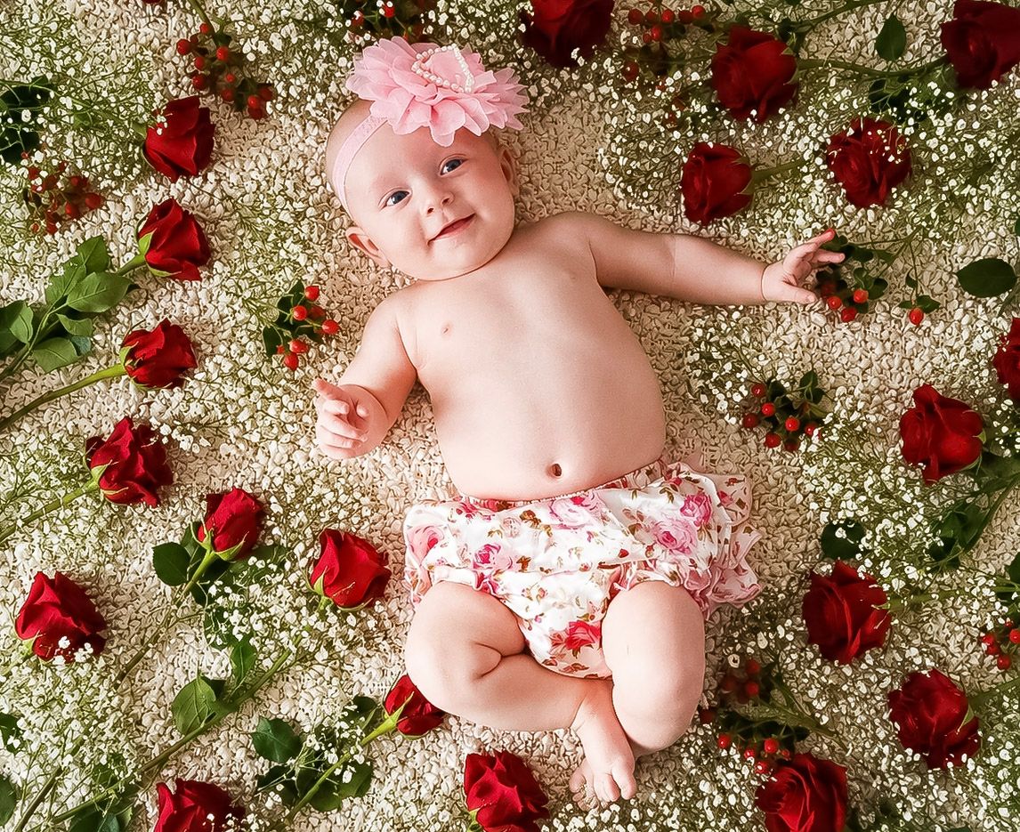 Baby girl smiling among red roses and gypsophila flowers