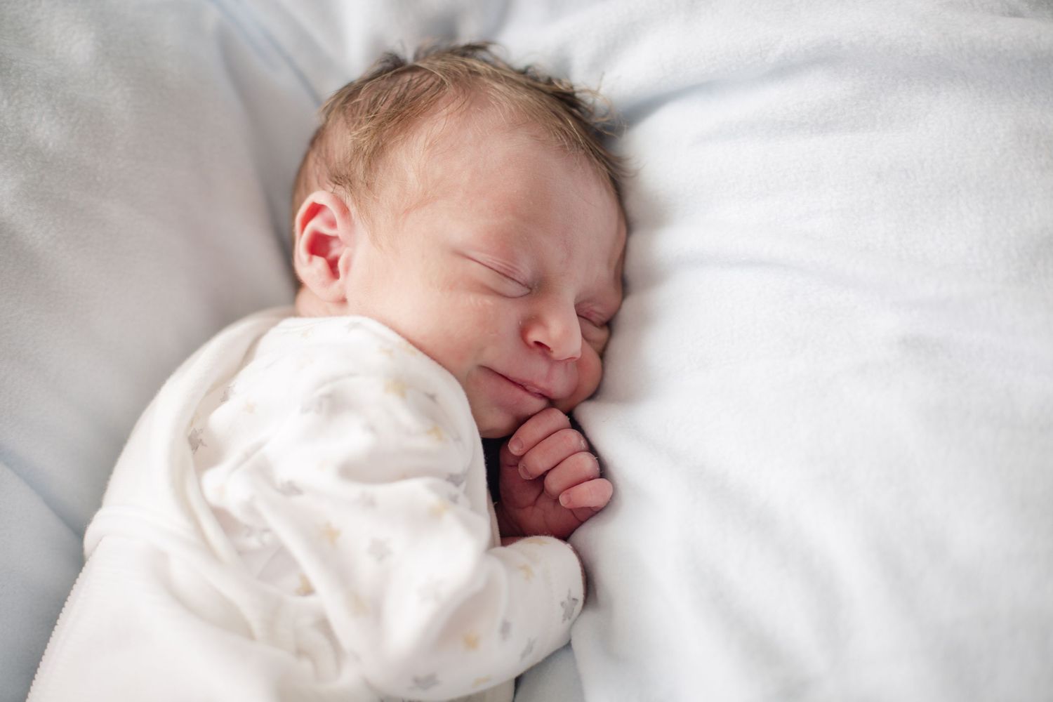 Sleeping newborn baby curled on a soft white blanket