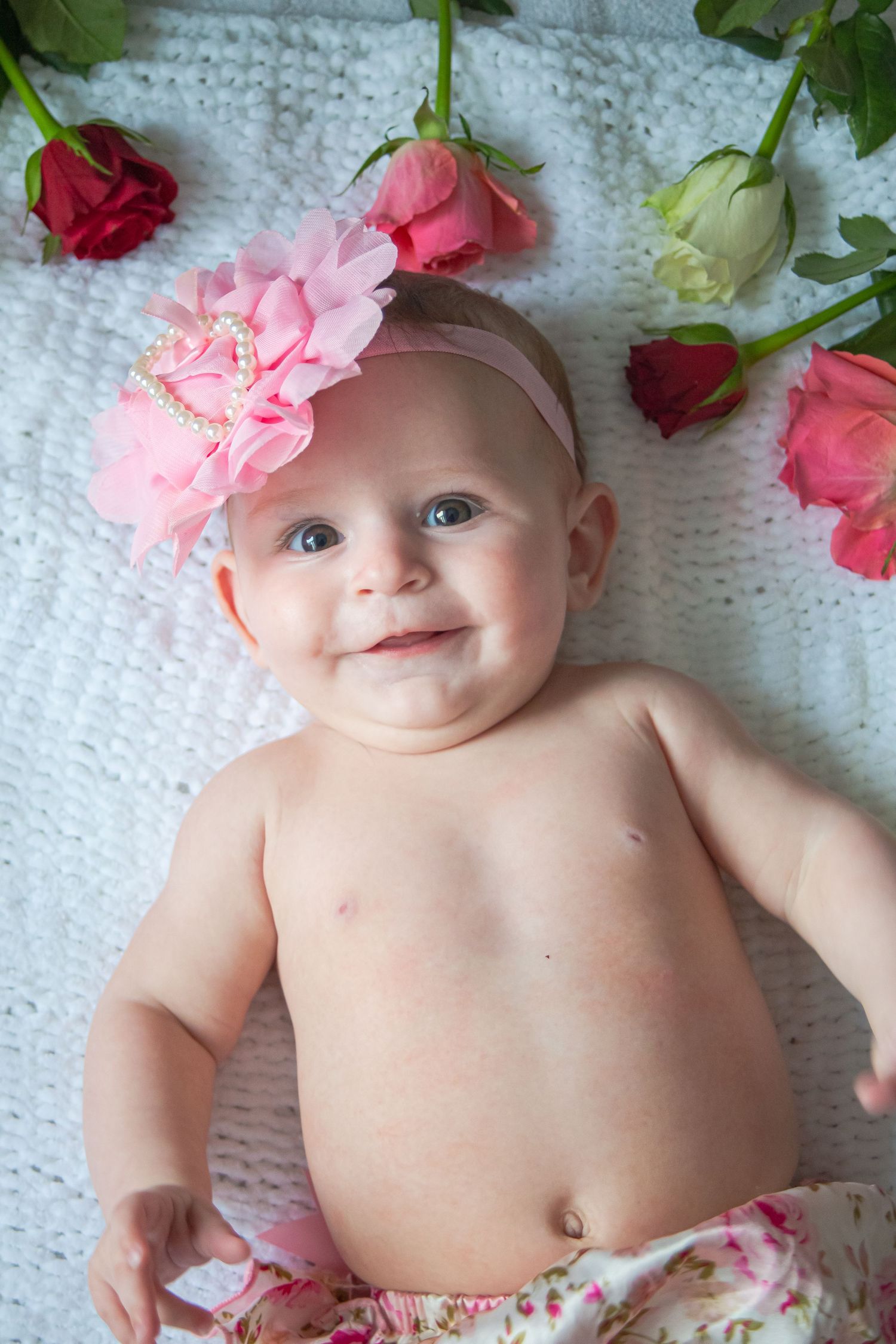 Baby girl wearing a pink flower headband surrounded by roses