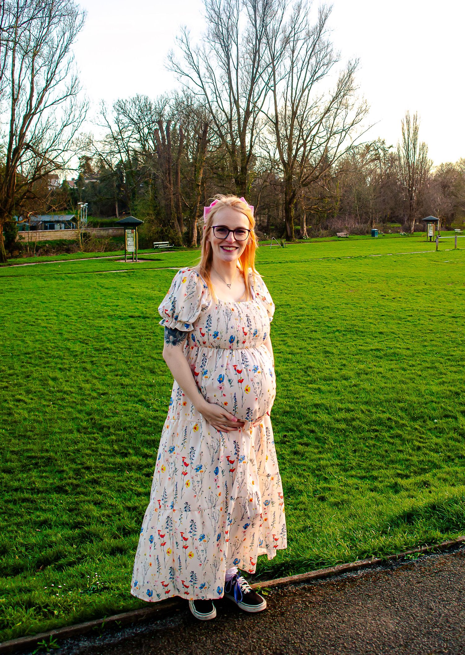 Full-length outdoor maternity portrait beside a green meadow