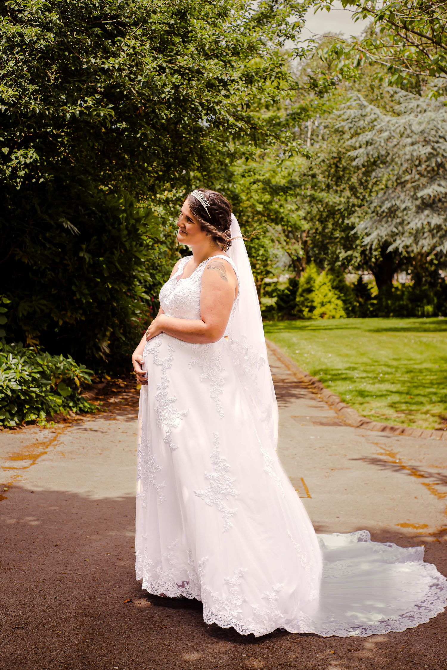 Portrait of the bride cuddling her pregnant bump, while standing in Sophia Gardens