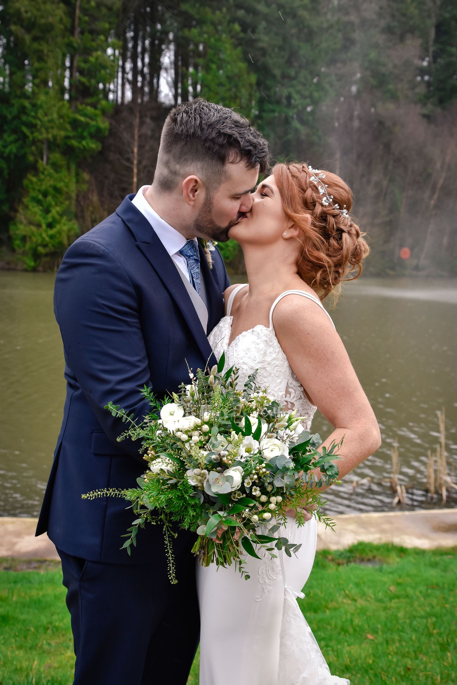 Bride and groom kissing while holding a white and green wedding bouquet