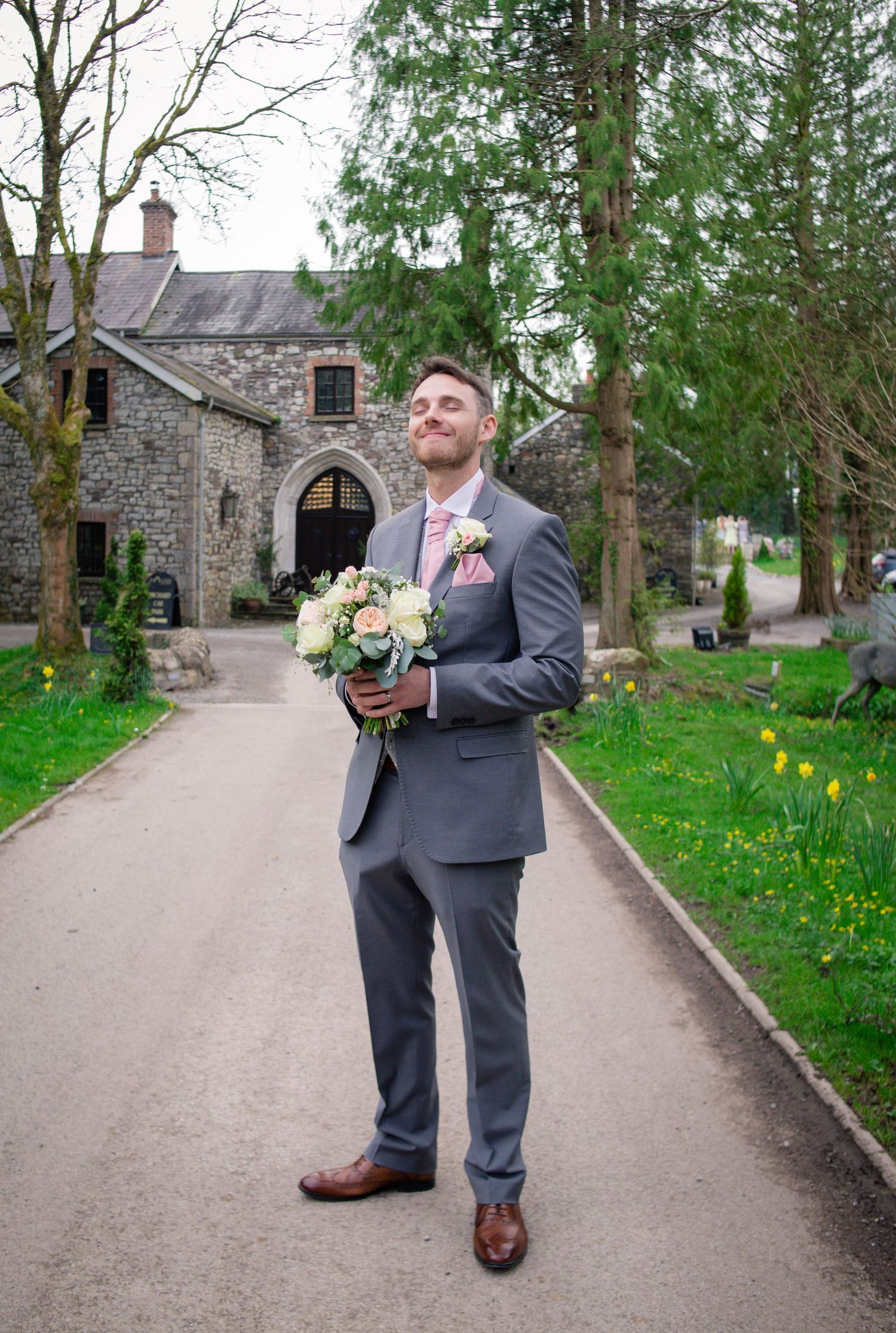 Groom holding the bridal bouquet outside Pencoed House in Bridgend