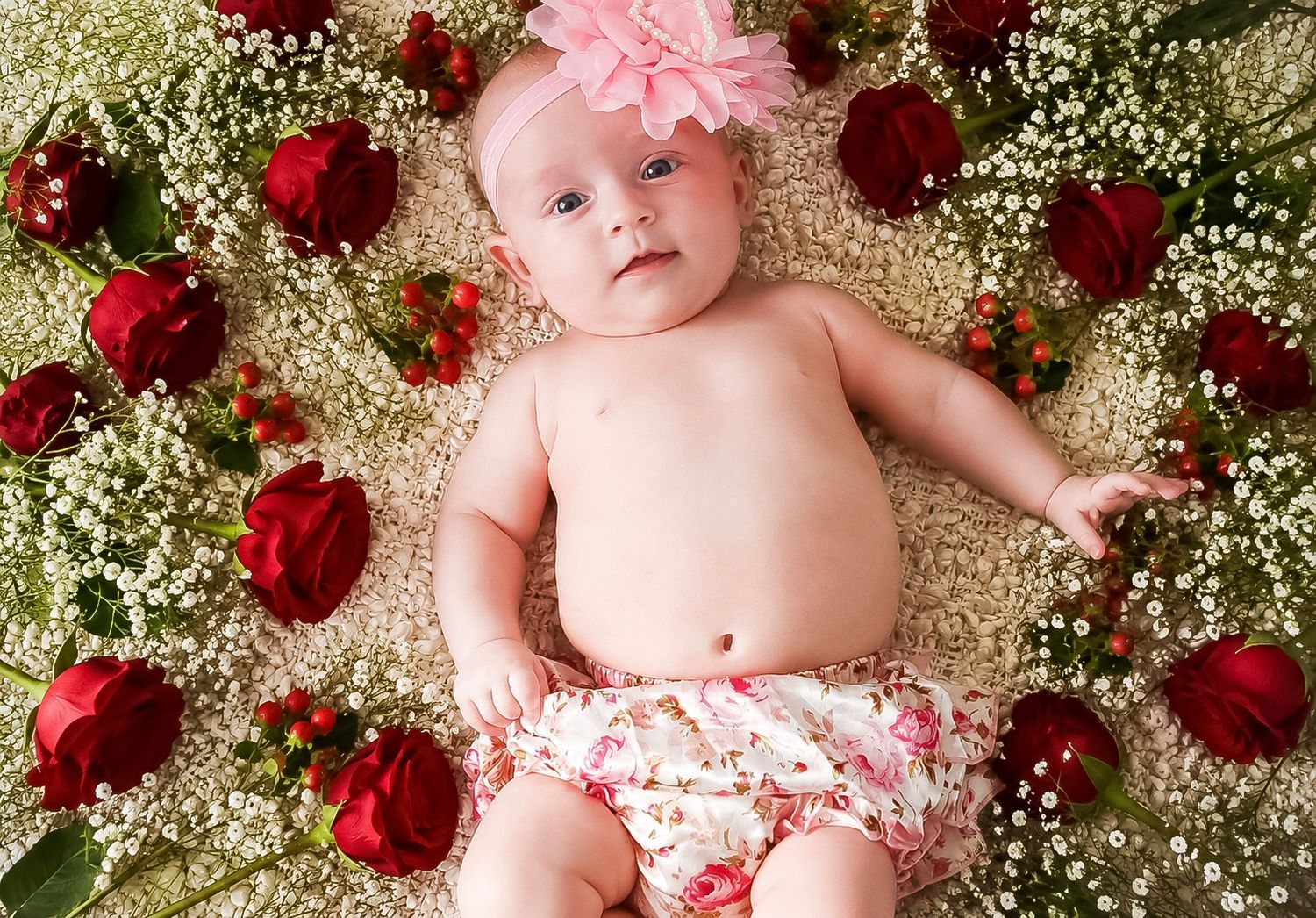 Baby girl wearing a pink flower headband surrounded by red roses