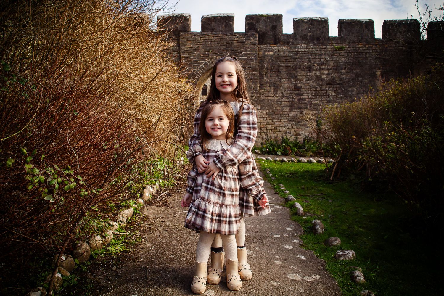 Two sisters standing together beside the historic stone walls at Southerndown