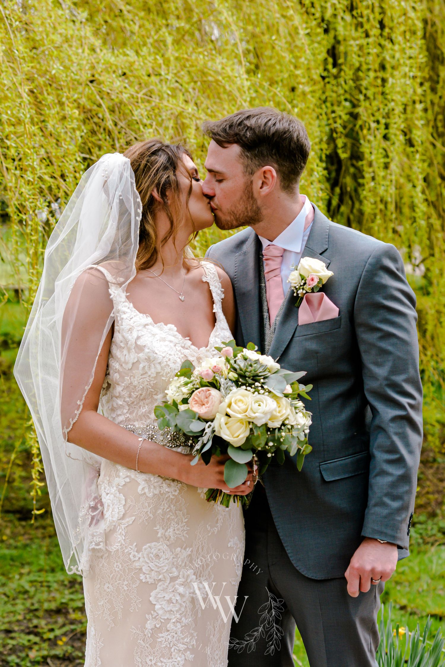 Bride and groom kissing beneath a willow tree at Pencoed House