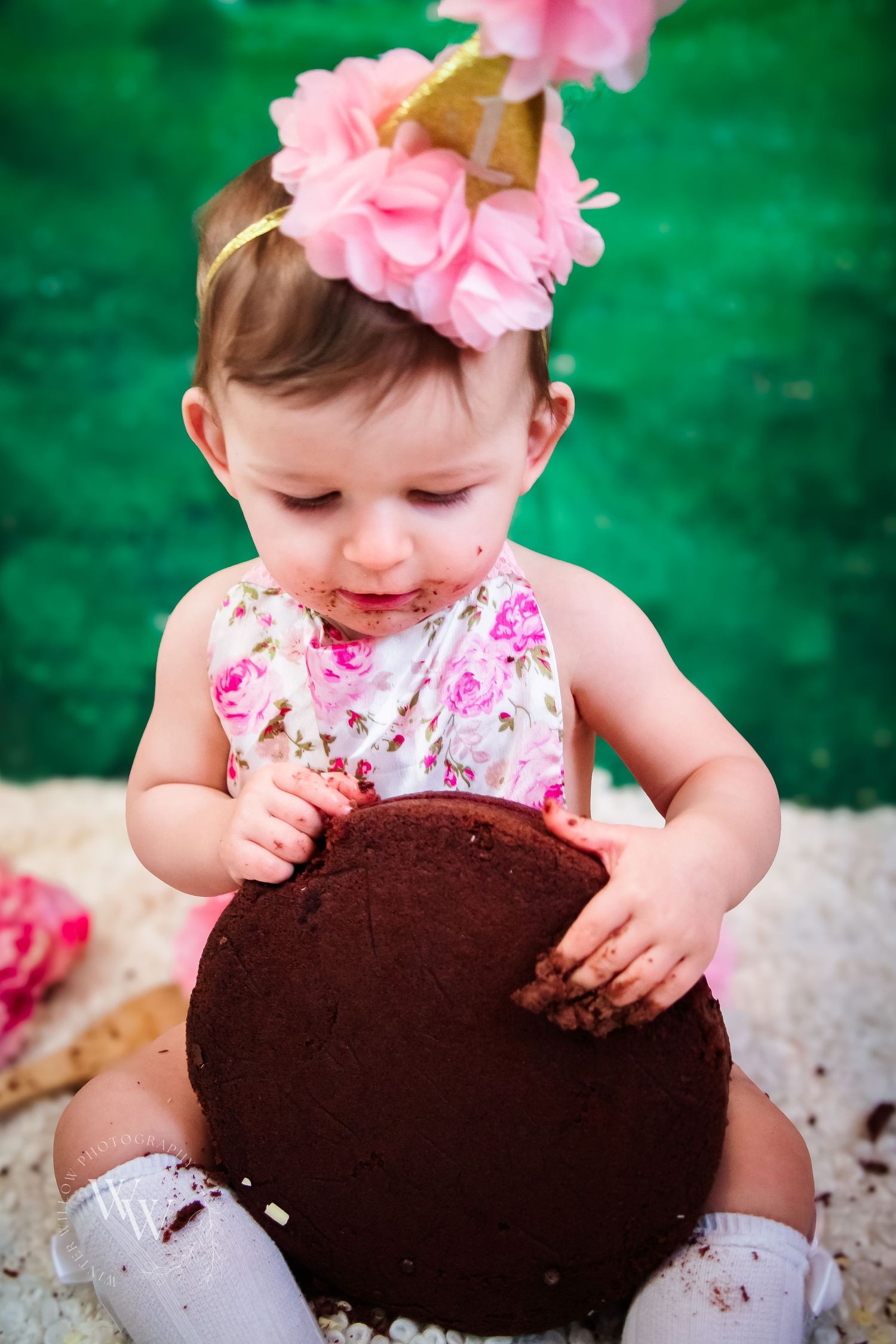 One-year-old girl exploring her chocolate birthday cake during a cake smash